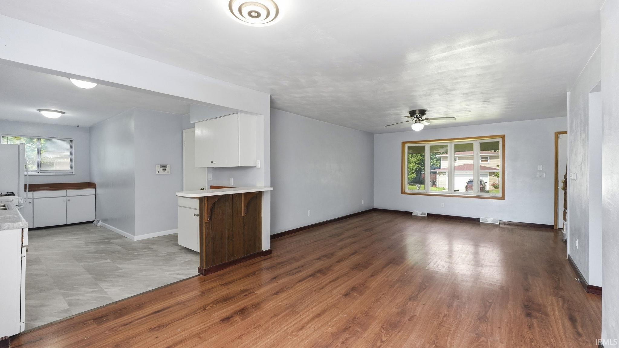 Spacious living area featuring wood-finish flooring, a ceiling fan, and a large multi-pane window