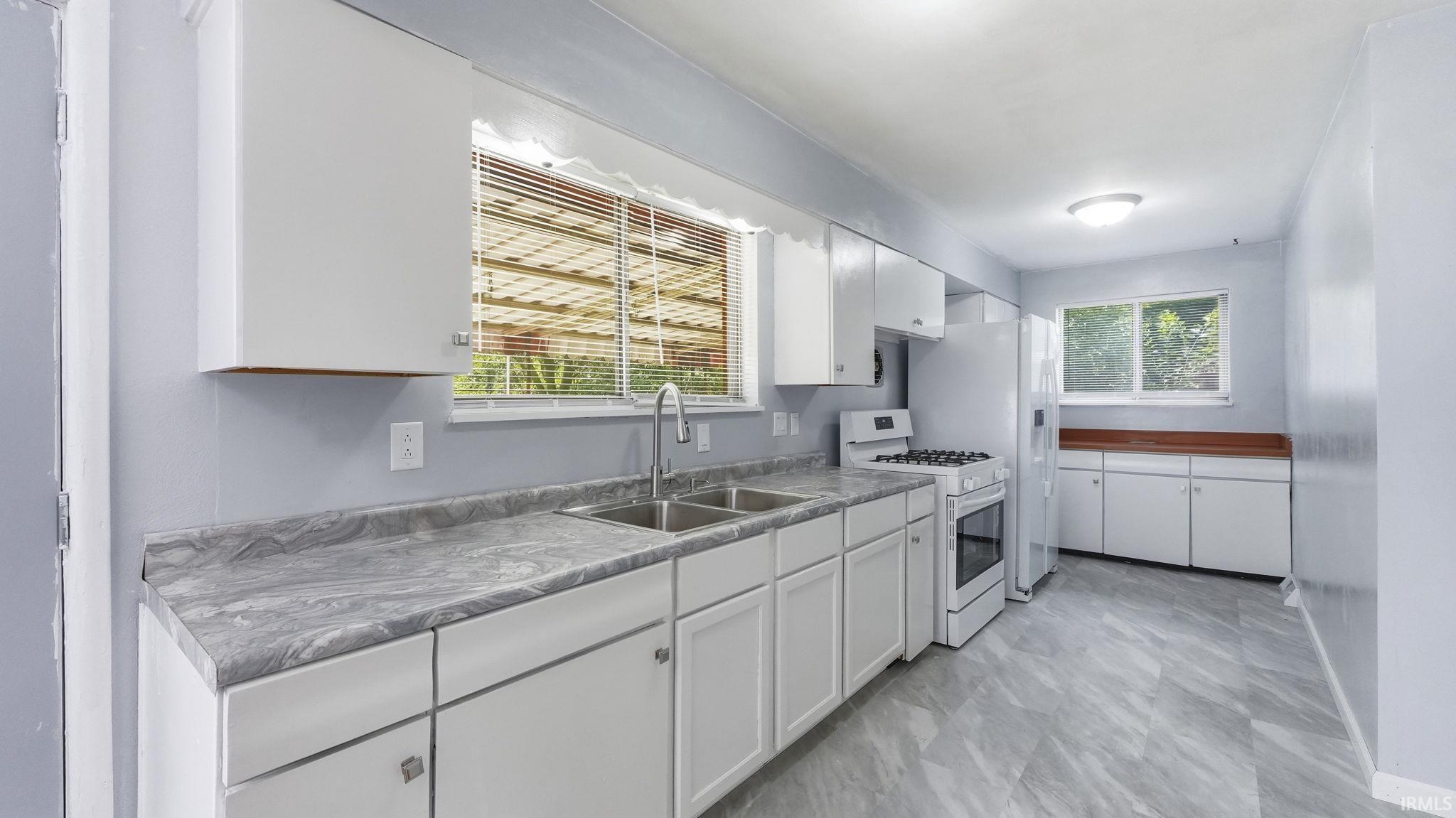 Kitchen featuring white cabinetry, gray marble-look countertops, a double-basin stainless steel sink, and light gray tile flooring