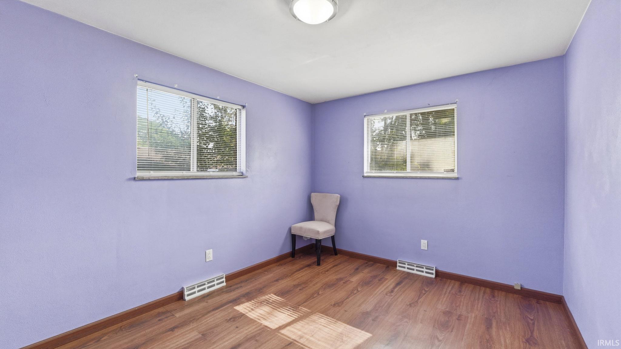 Room featuring two windows with blinds, wood-finish flooring, and a flush-mount ceiling light