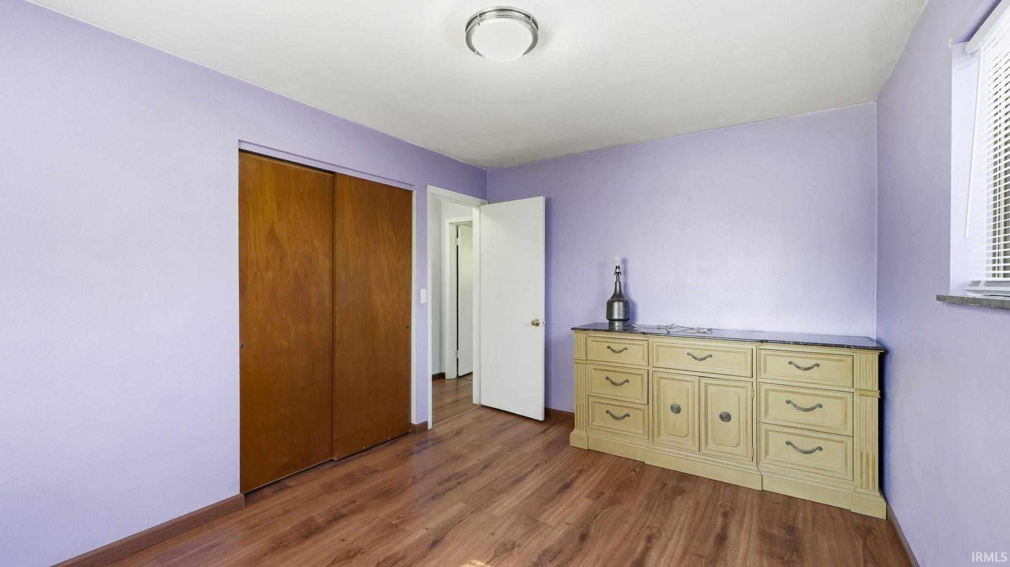 Room featuring wood-finish flooring, a double-door closet, a window with horizontal blinds, and a flush-mount ceiling light