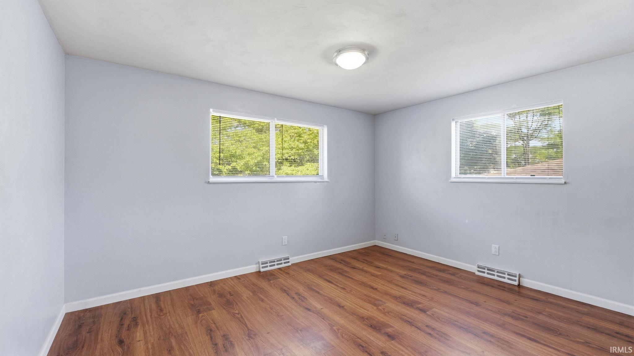 Room featuring wood-finish flooring, light blue walls, white trim, and two windows