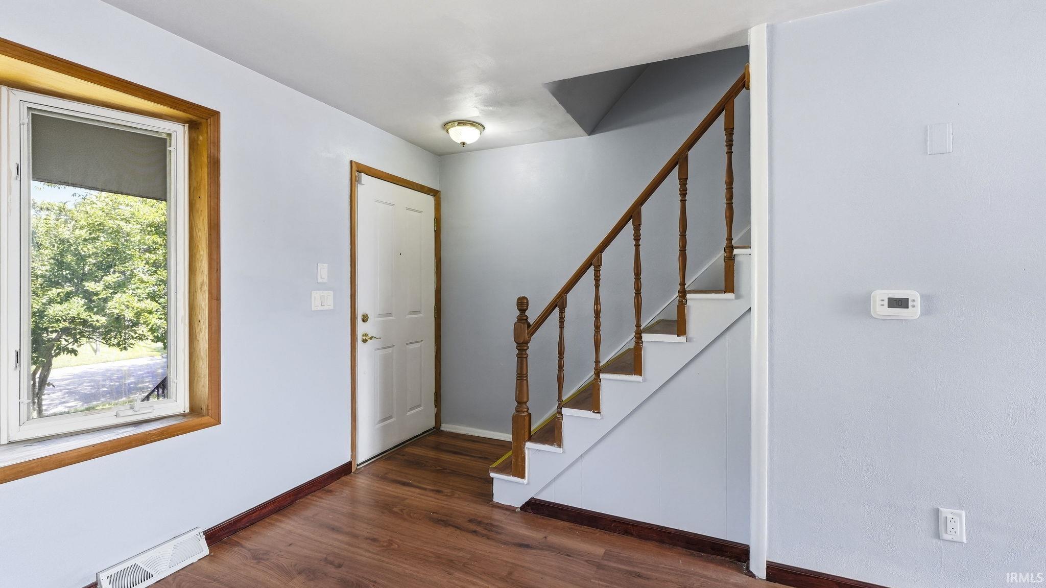 Entryway featuring wood-finish flooring, a white front door with wood trim, and a staircase with a wood handrail and balusters