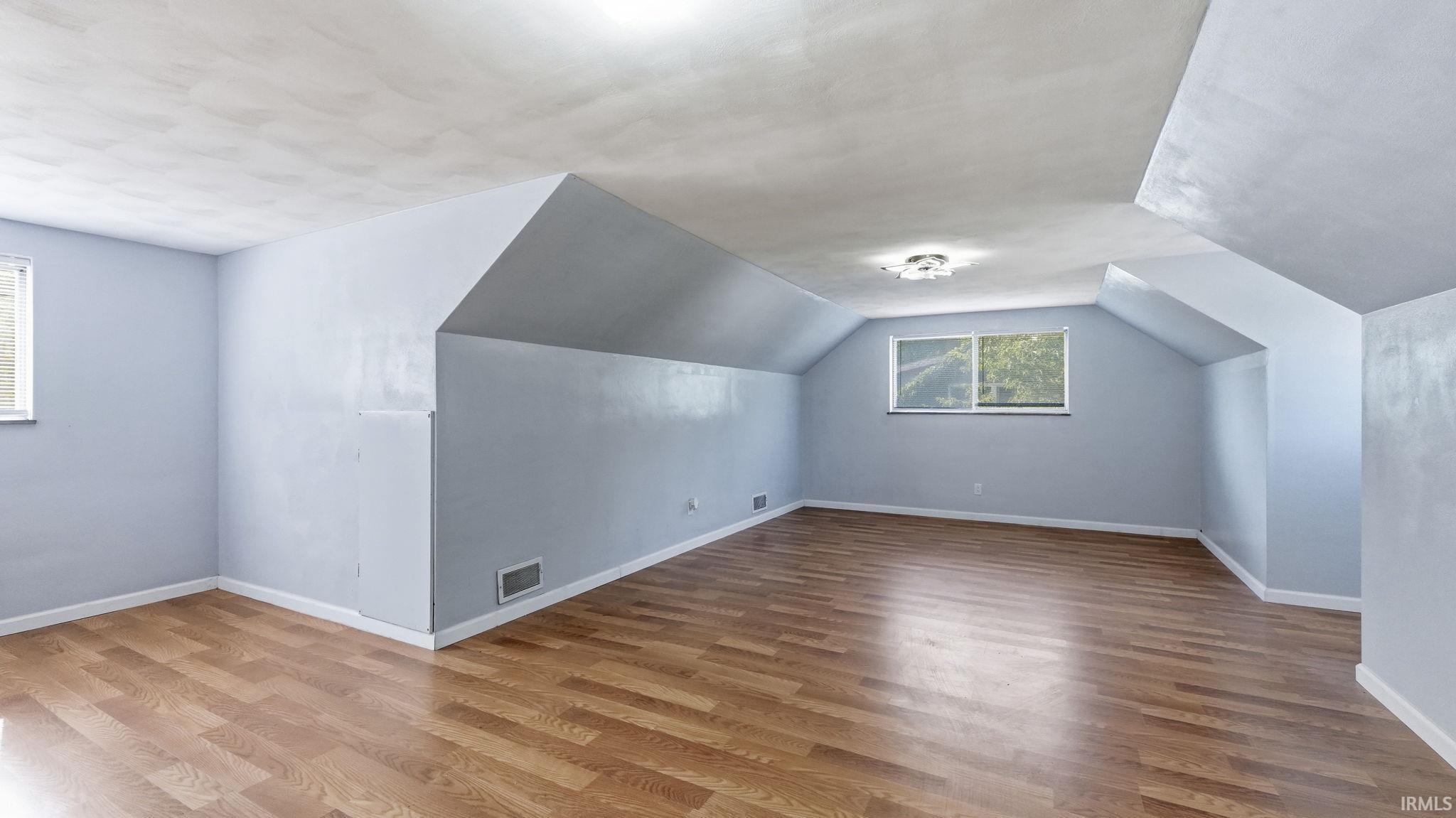 Spacious room featuring wood-finish flooring, light blue walls, and a multi-pane window