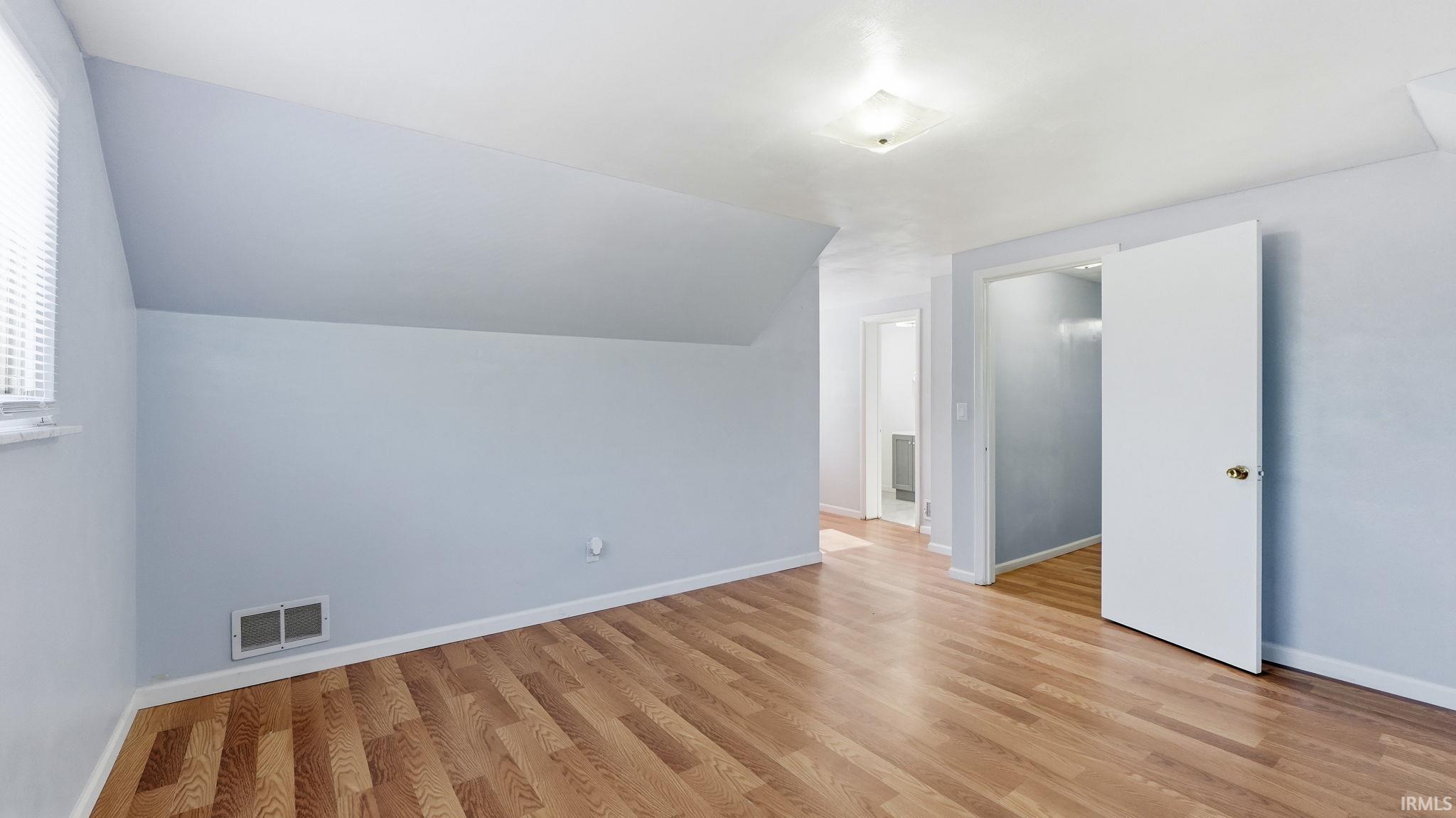 Room featuring wood-finish flooring, light blue wall paint, white trim, and a sloped ceiling