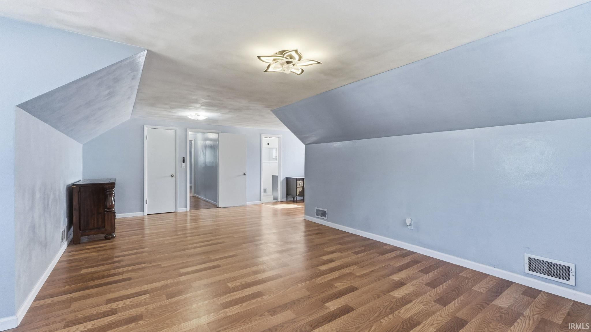 Spacious room featuring wood-finish flooring, light blue walls, a textured ceiling, built-in lighting, and white trim