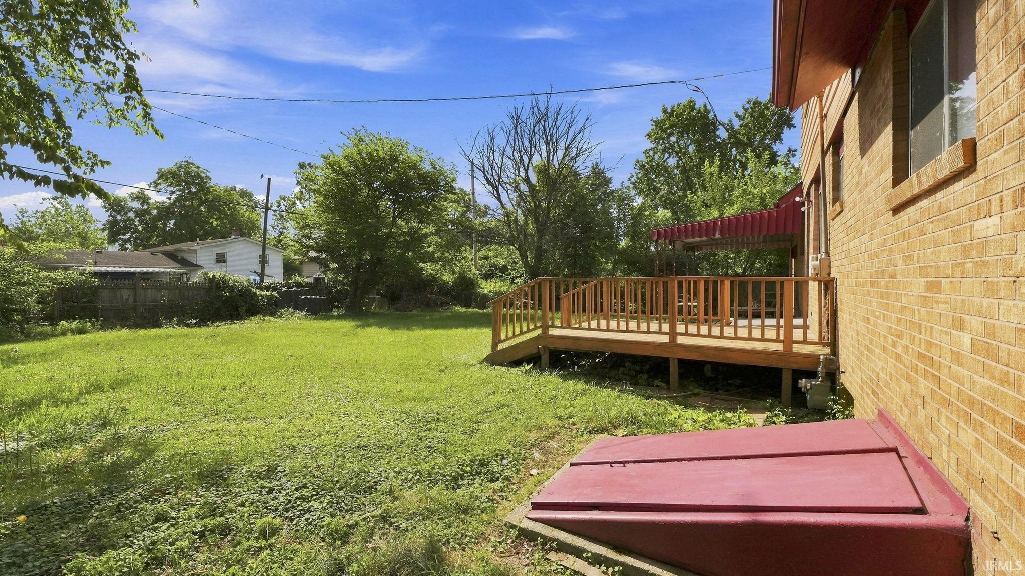 Expansive backyard featuring a large wooden deck with railing, a red fabric awning, and a brick exterior