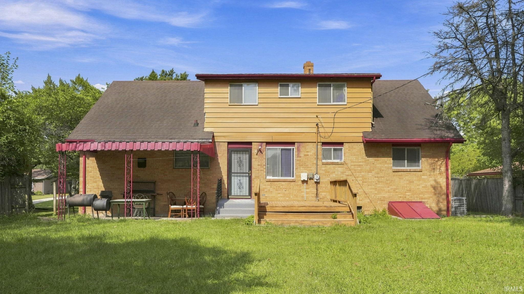 Expansive backyard featuring a manicured lawn, brick exterior, wood-finish siding, covered patio, and a wooden deck