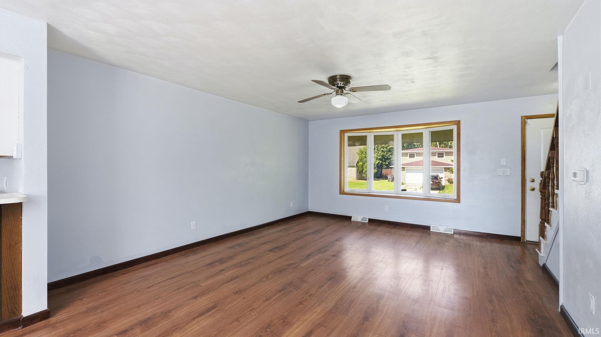 Spacious interior featuring wood-finish flooring, a multi-pane window with wood trim, and a ceiling fan with integrated lighting