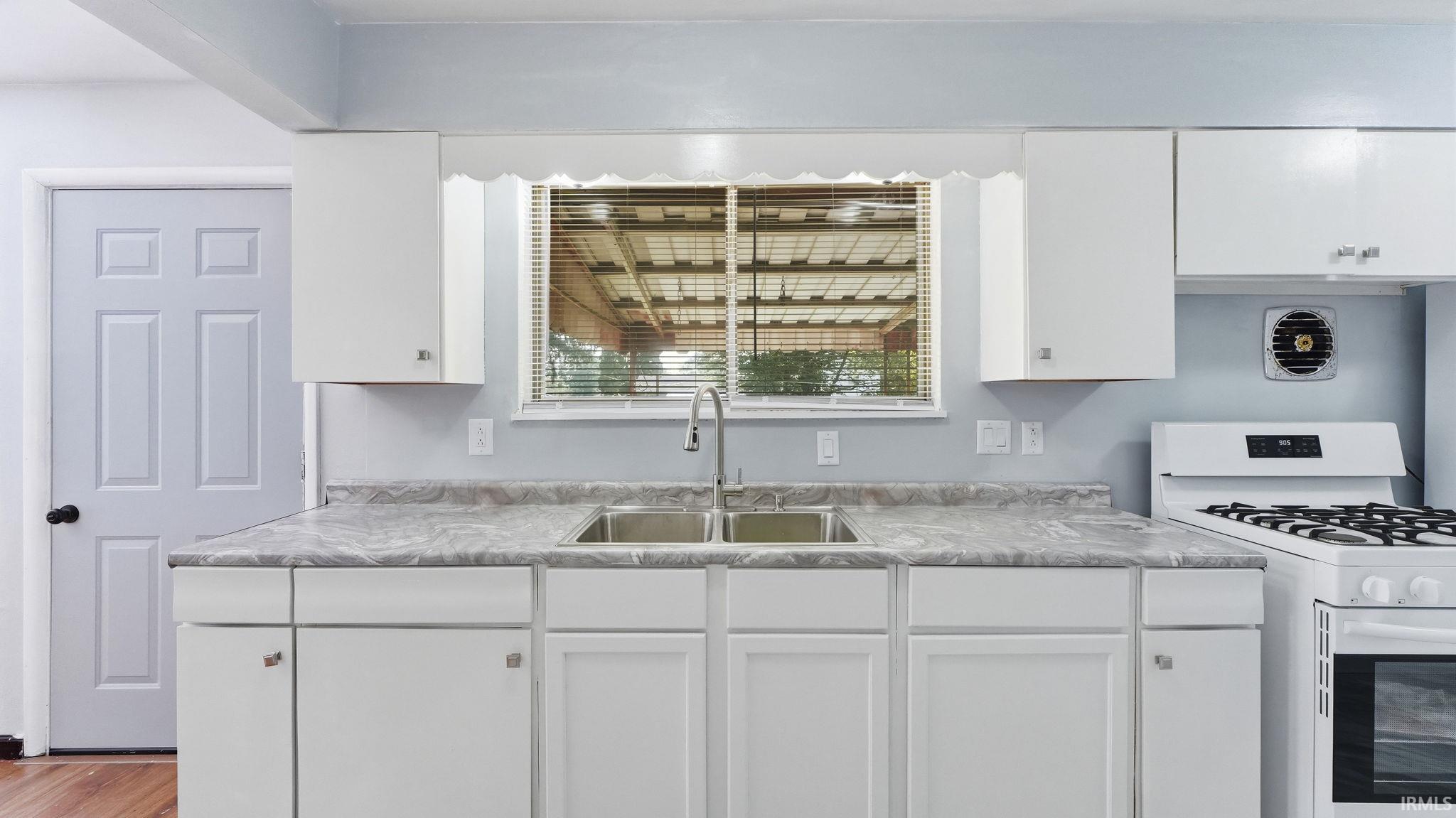Kitchen featuring white cabinetry, a double basin stainless steel sink with a high-arc faucet, and gray patterned countertops