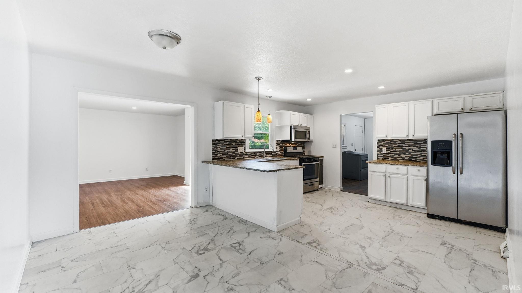 Bright kitchen featuring white cabinetry, stone-finish countertops, stainless steel appliances, and large format marble-look flooring