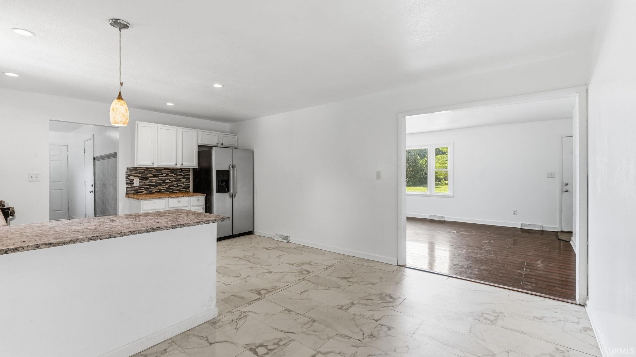 Open-concept kitchen featuring an eat-at counter, stainless steel appliances, white cabinetry, and a patterned tile backsplash
