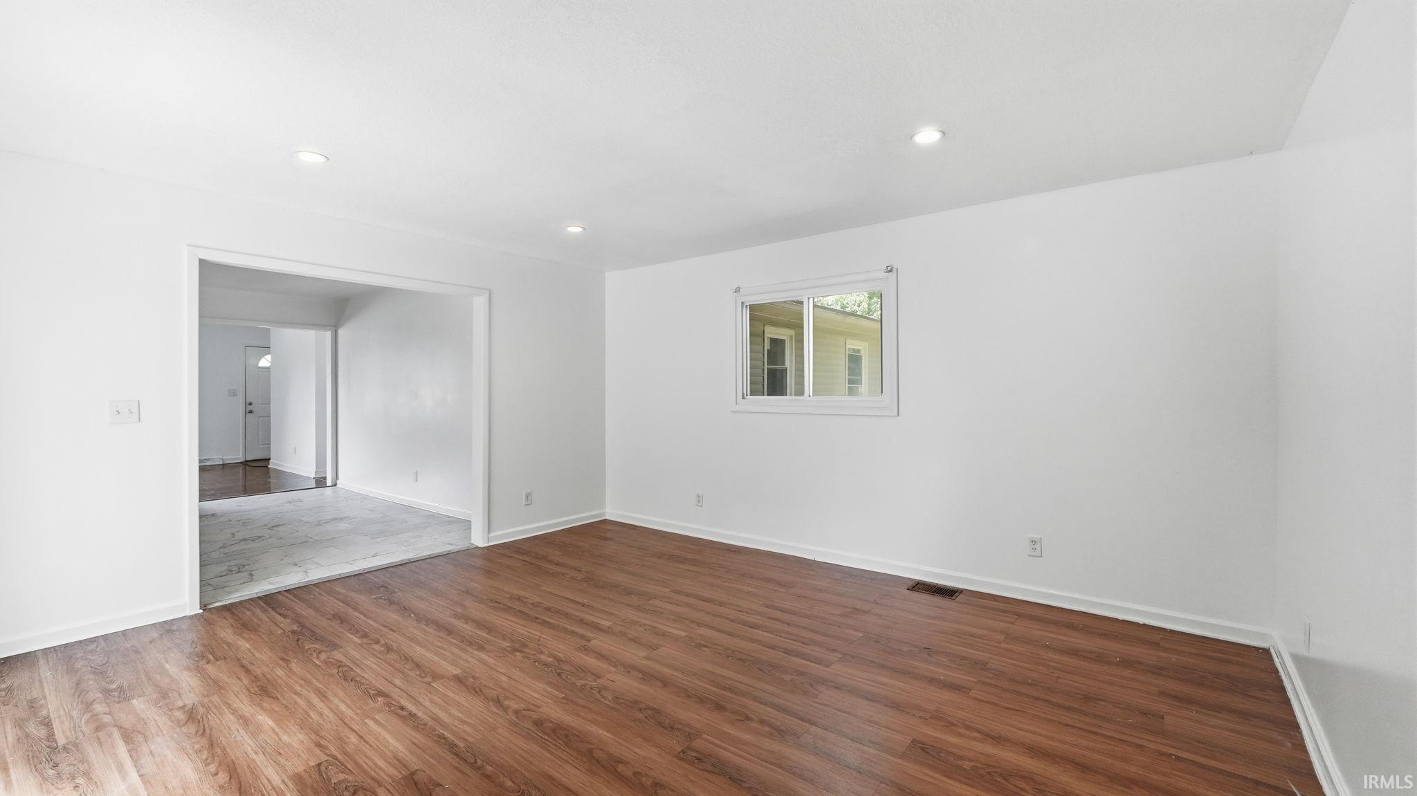 Living area featuring wood-finish flooring, recessed lighting, white walls, and a window with white trim