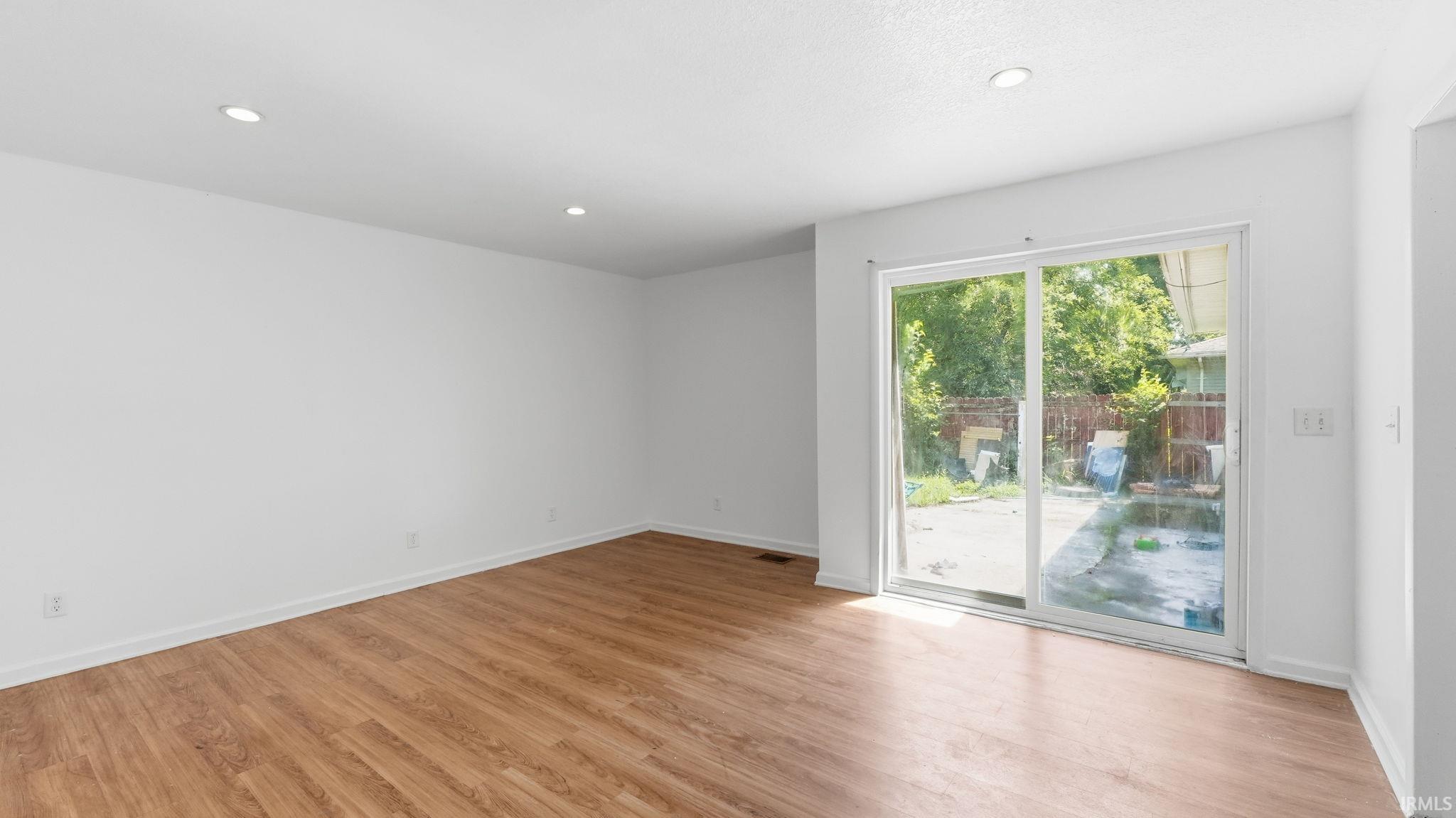 Spacious room featuring wood-finish flooring, white baseboards, recessed lighting, and a white sliding glass door