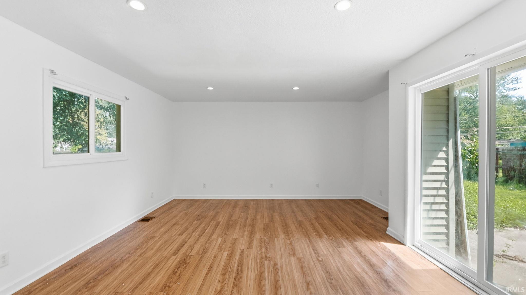 Spacious room featuring wood-finish flooring, white walls, and recessed lighting
