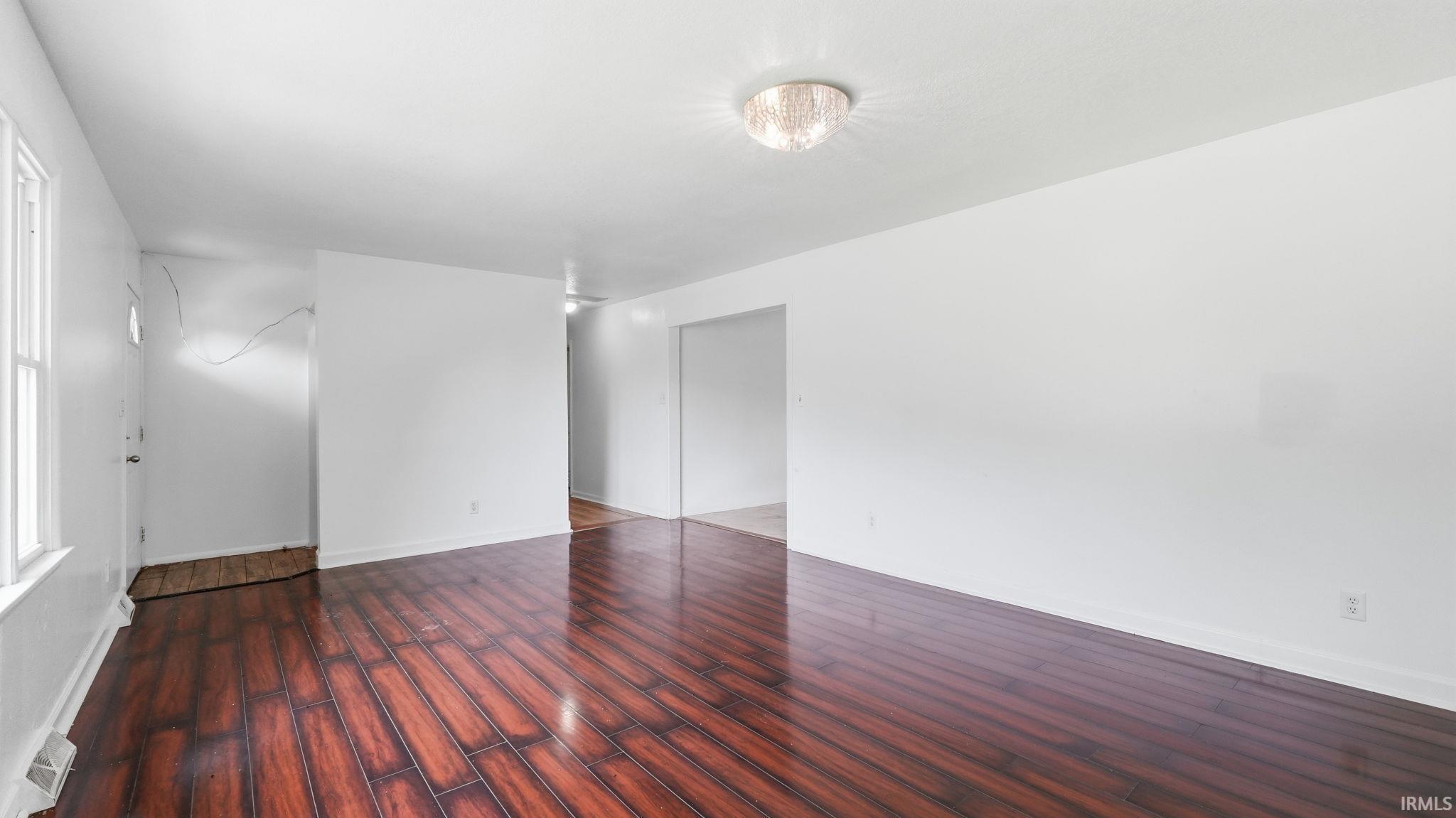 Spacious room featuring wood-finish flooring, white walls, and a contemporary ceiling light fixture