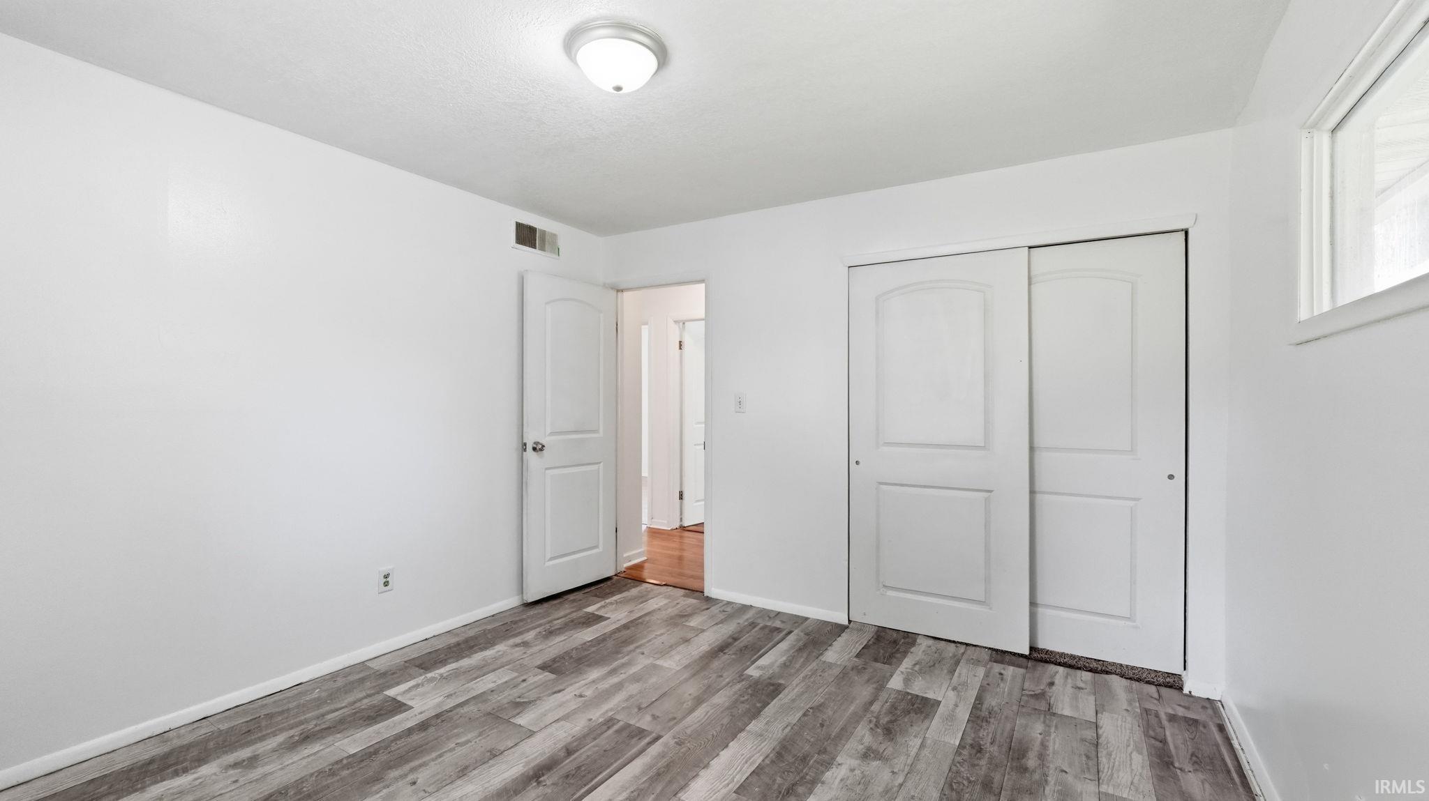 Spacious room featuring wood-finish flooring, white walls, and a ceiling-mounted light fixture