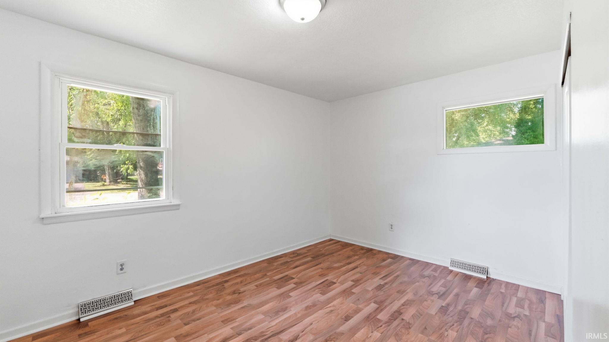 Interior room featuring wood-finish flooring, two windows with white trim, white baseboards, and a white ceiling with a flush-mount light fixture