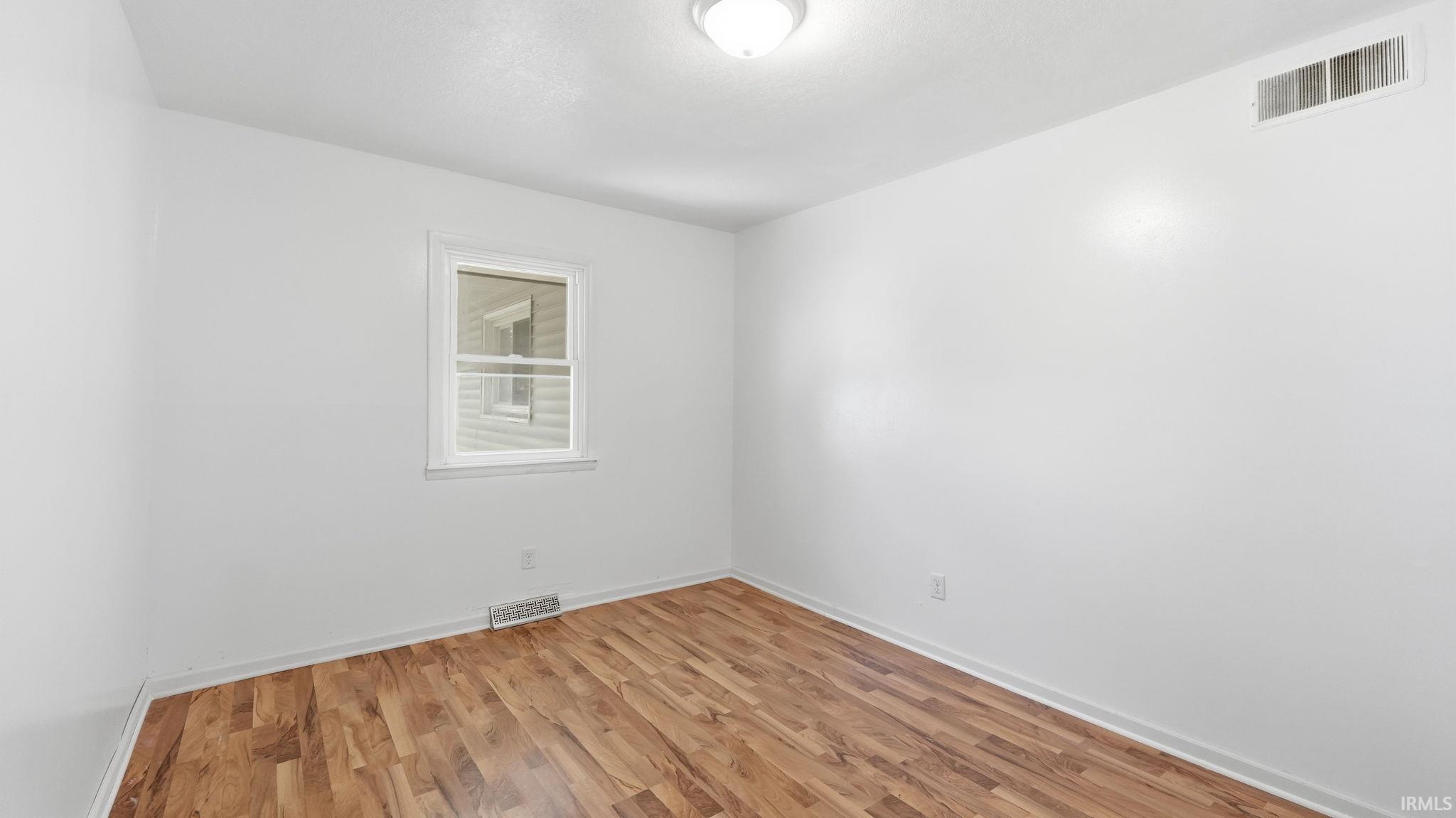 Bright interior space featuring wood-finish flooring, white walls, and a single window with white trim