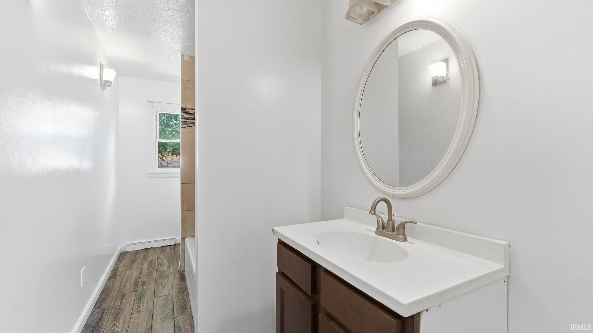 Bathroom vanity featuring a white countertop with an integrated sink, brushed nickel faucet, and an oval framed mirror