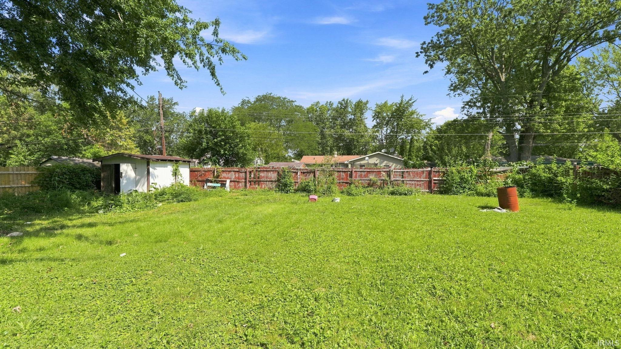 Expansive grassy yard featuring a wood privacy fence, established perimeter trees, and a detached storage shed