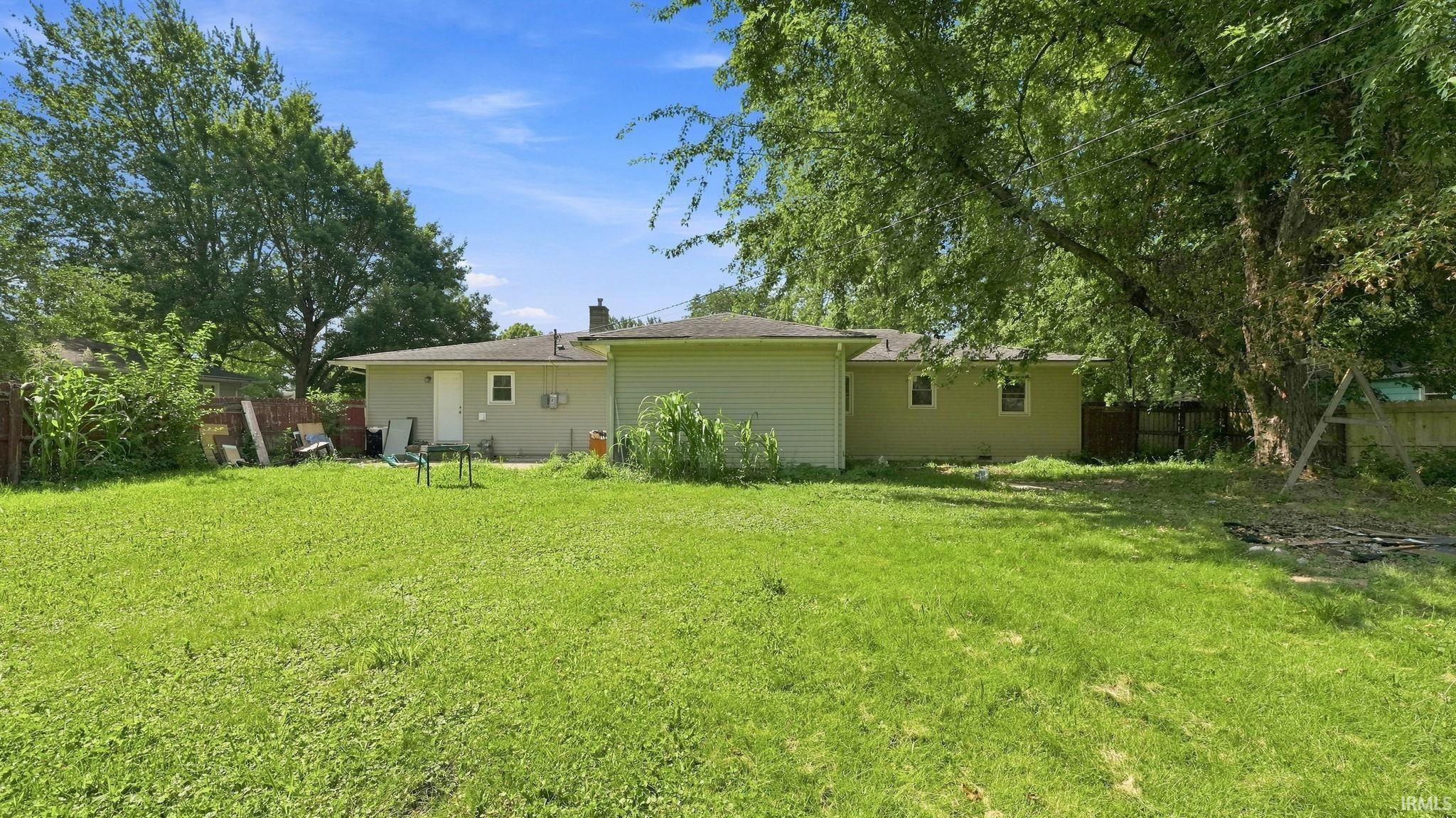 Expansive green lawn with mature trees and a partial wood fence