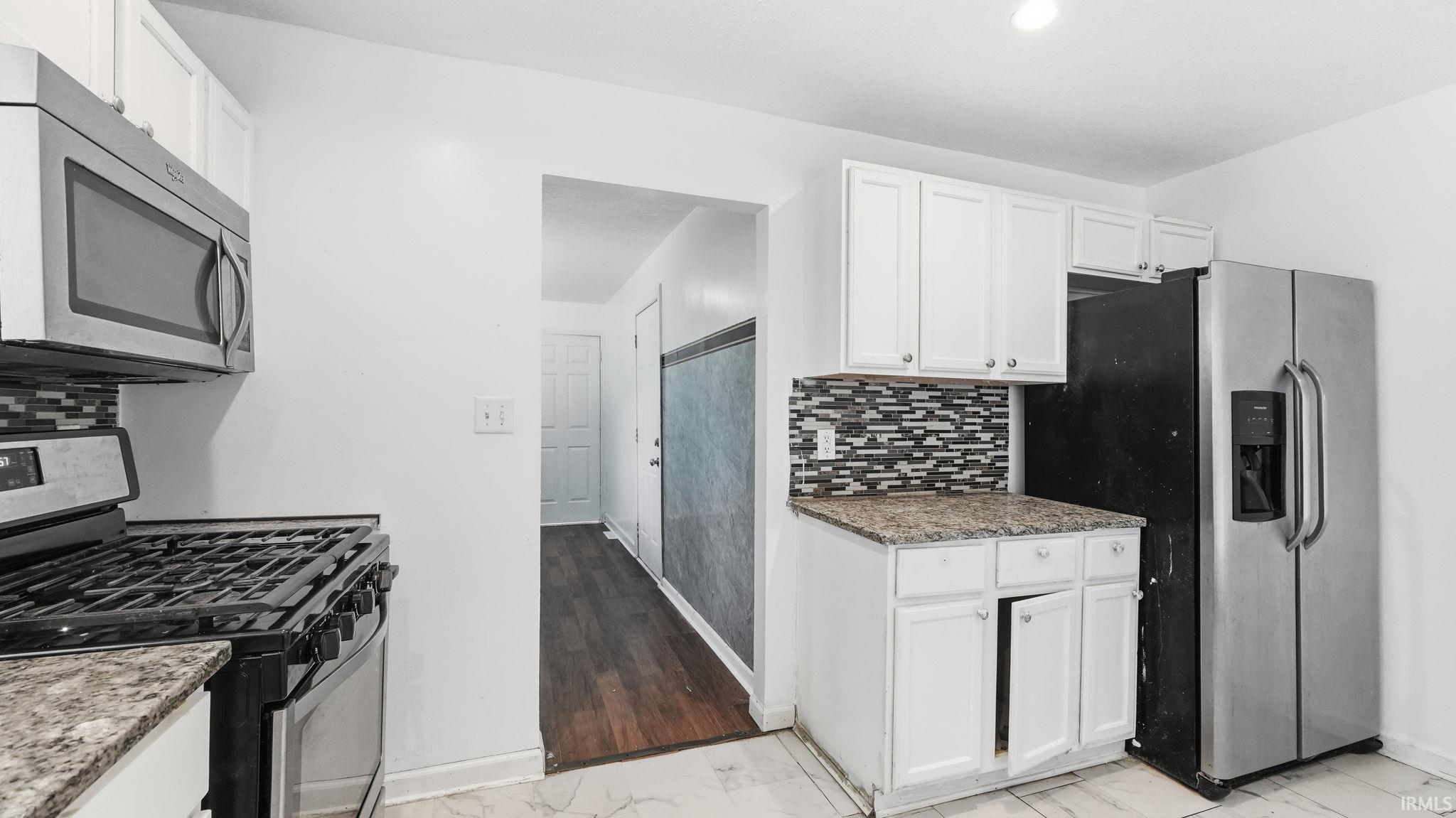 Kitchen featuring white cabinetry, stone-finish countertops, and mosaic tile backsplash