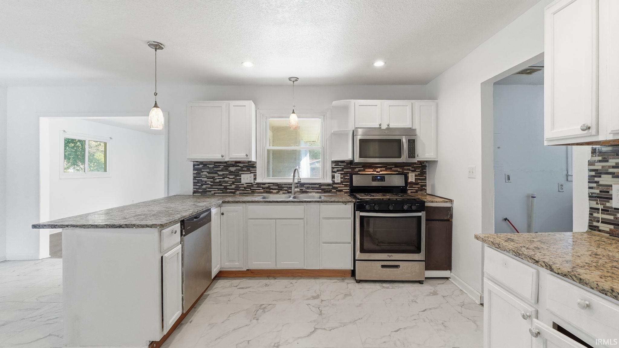 Kitchen featuring white cabinetry, granite countertops, stainless steel appliances, a mosaic tile backsplash, and light-colored flooring