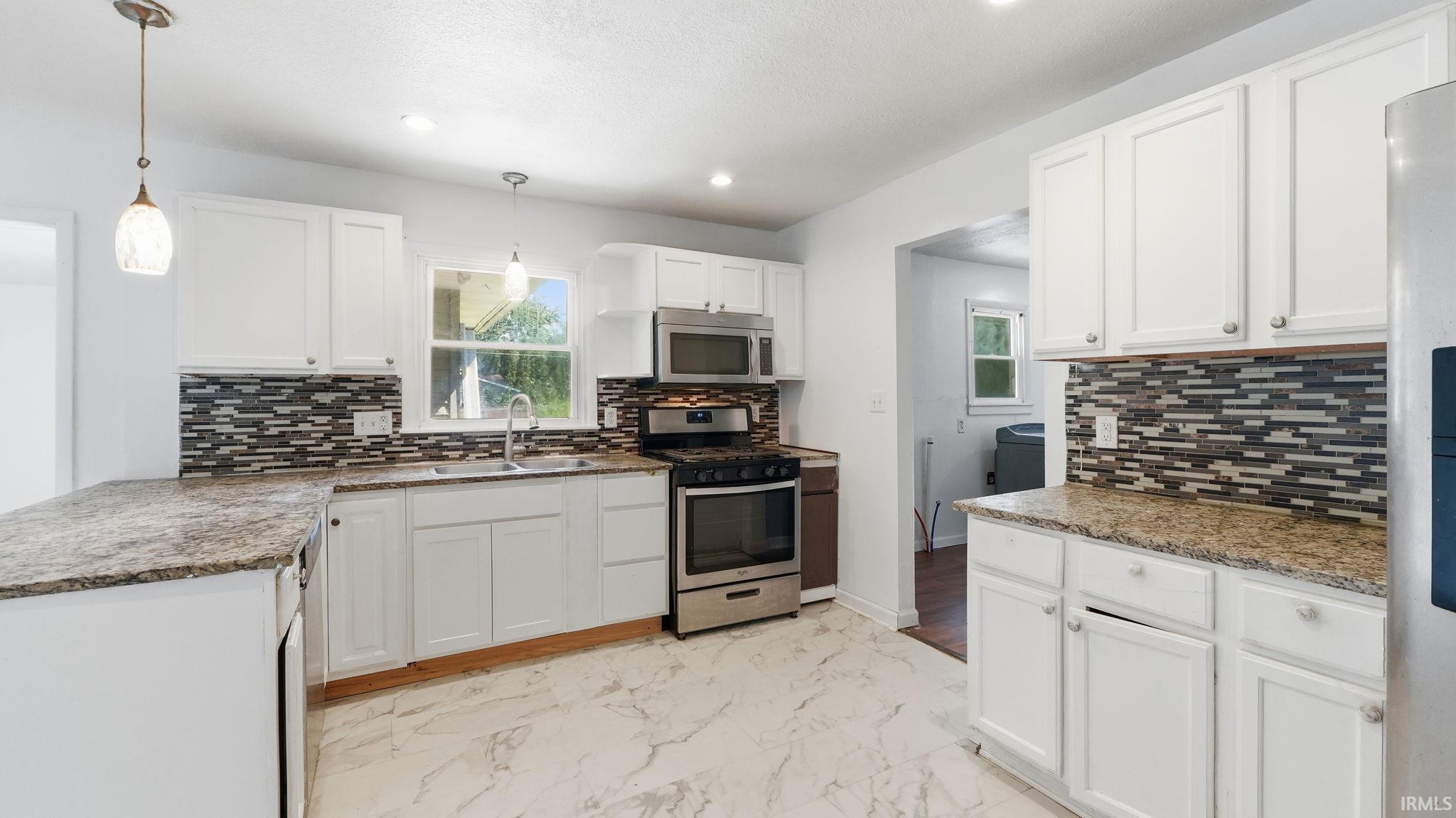Kitchen featuring white cabinetry, granite-finish countertops, stainless steel appliances, a mosaic tile backsplash, and white marble-look flooring