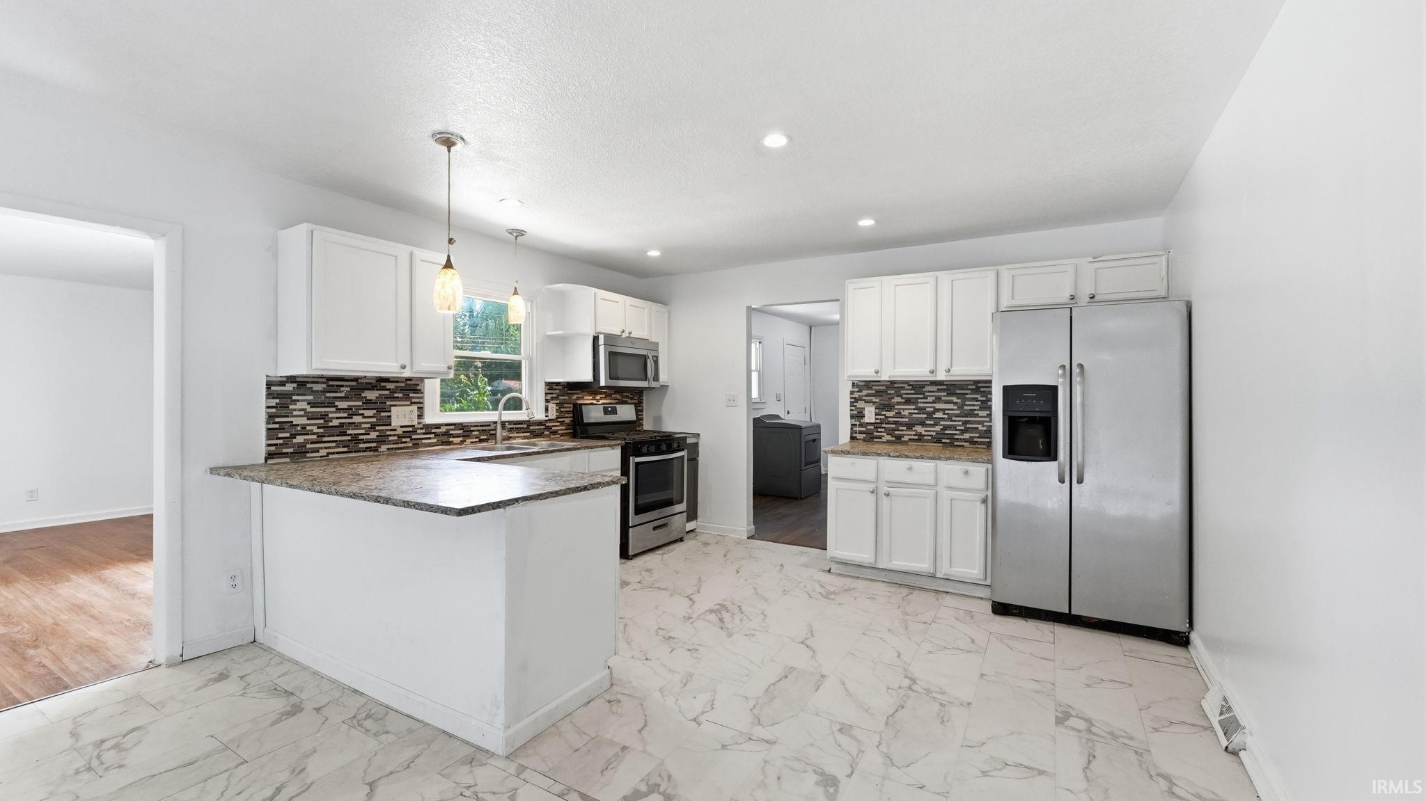 Kitchen featuring white cabinetry, stone-finish countertops, stainless steel appliances, mosaic tile backsplash, and light-tone marble-style flooring
