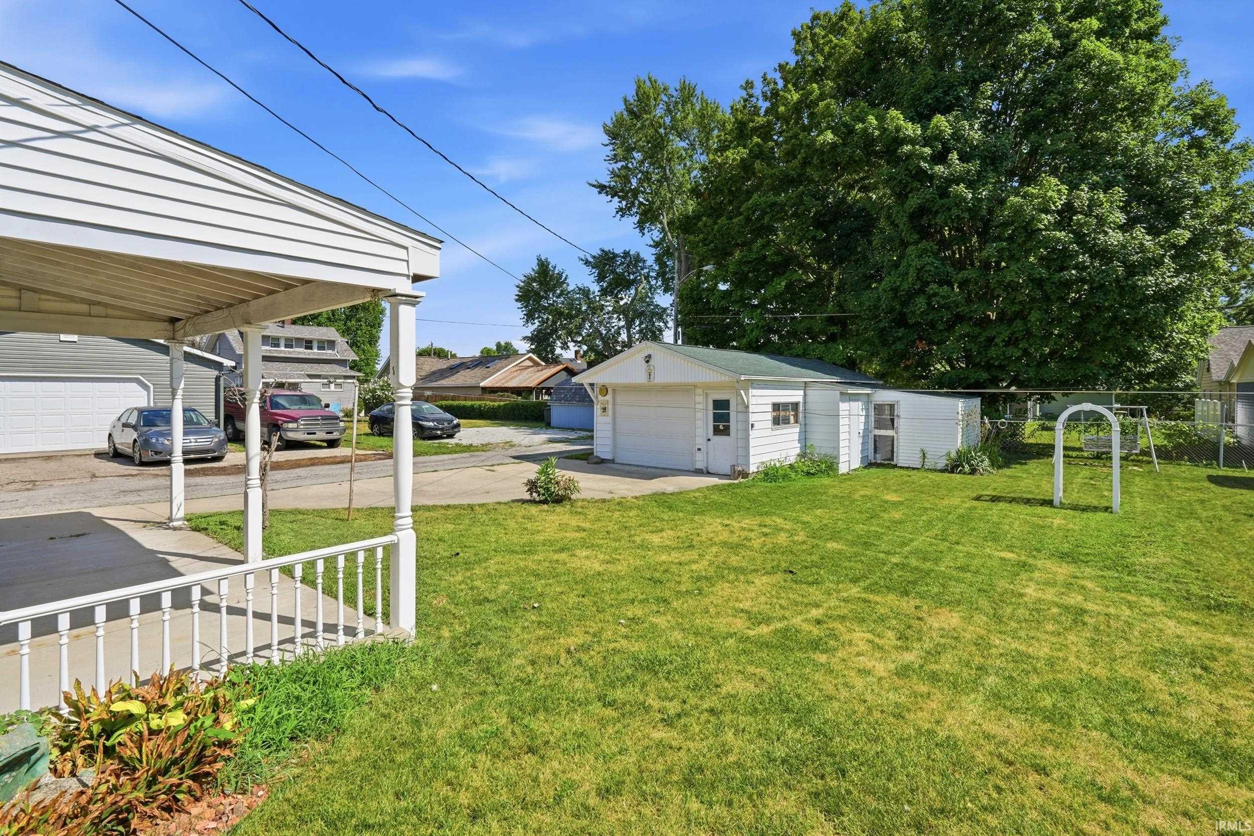 Expansive backyard featuring a detached garage with an overhead door, an additional outdoor storage shed, and a covered porch with white railing