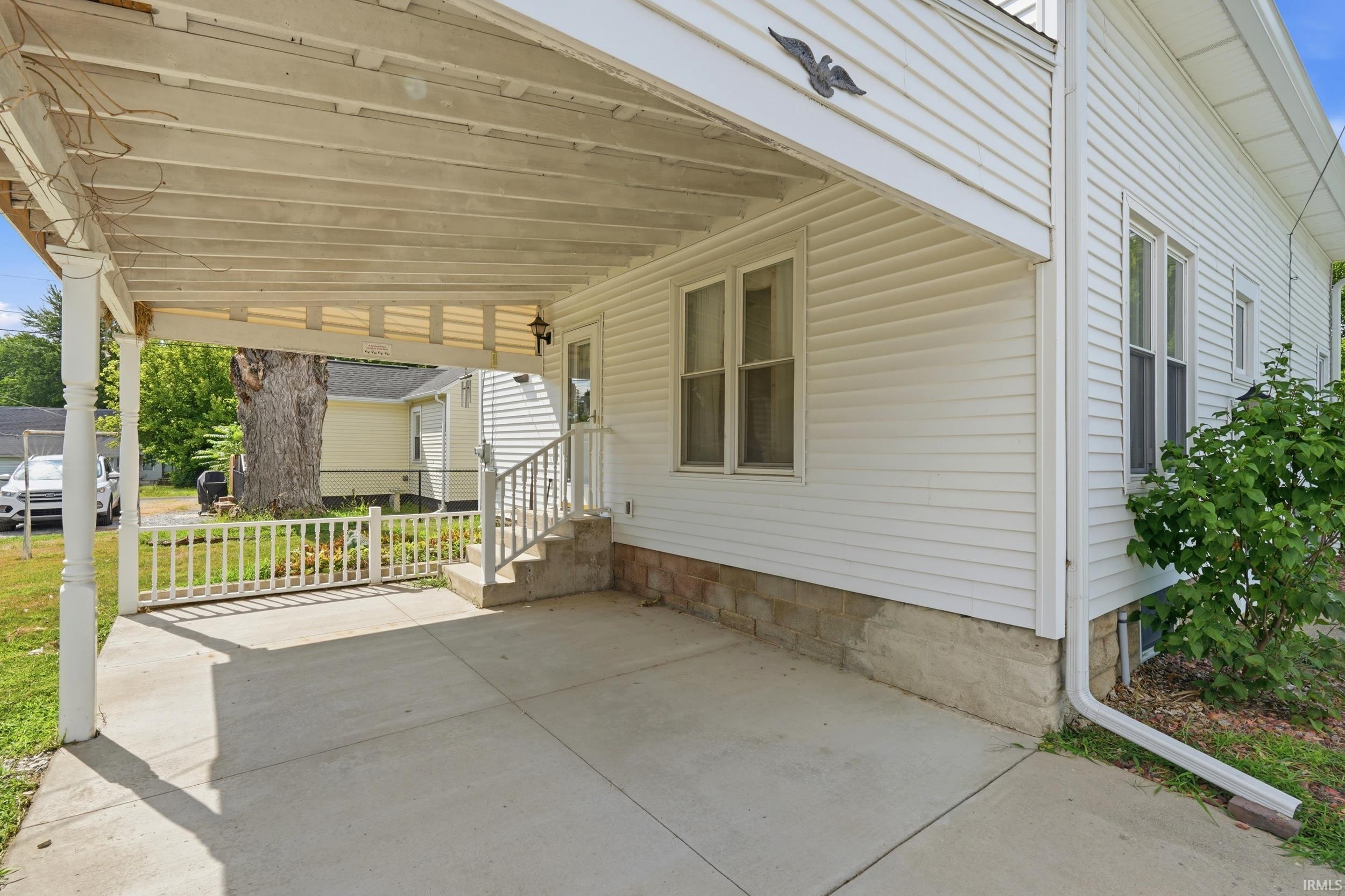 Covered concrete patio with white wood railing, steps, and house siding
