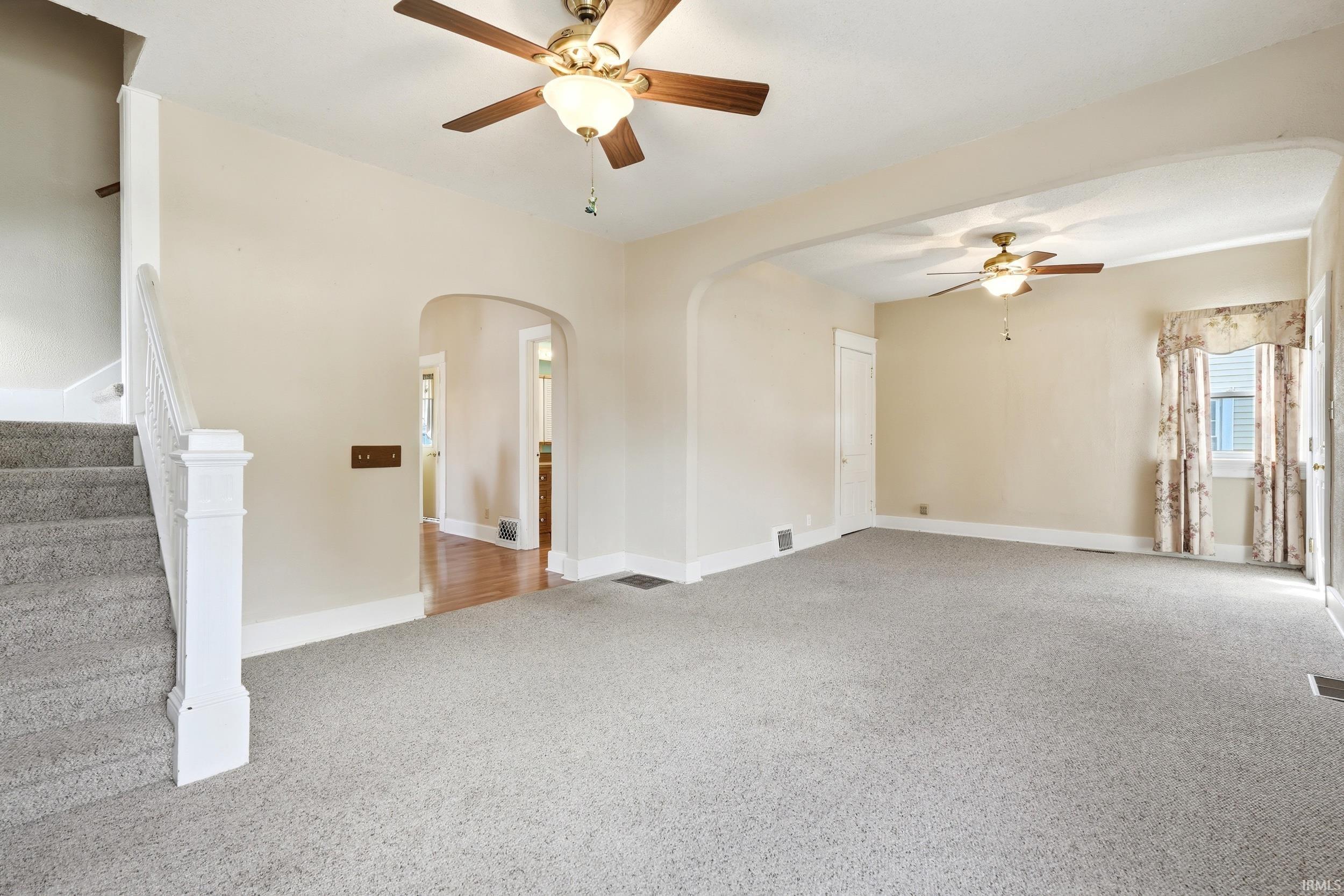 Spacious living area featuring light-toned walls, ceiling fans with integrated lighting, and plush carpeting