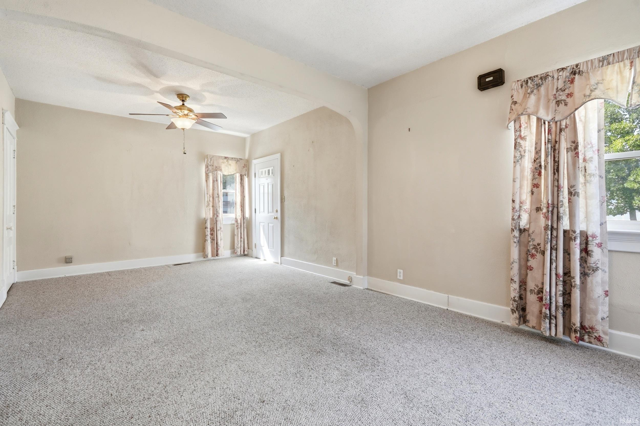 Spacious room with light-toned walls, ceiling fan, and carpeted flooring