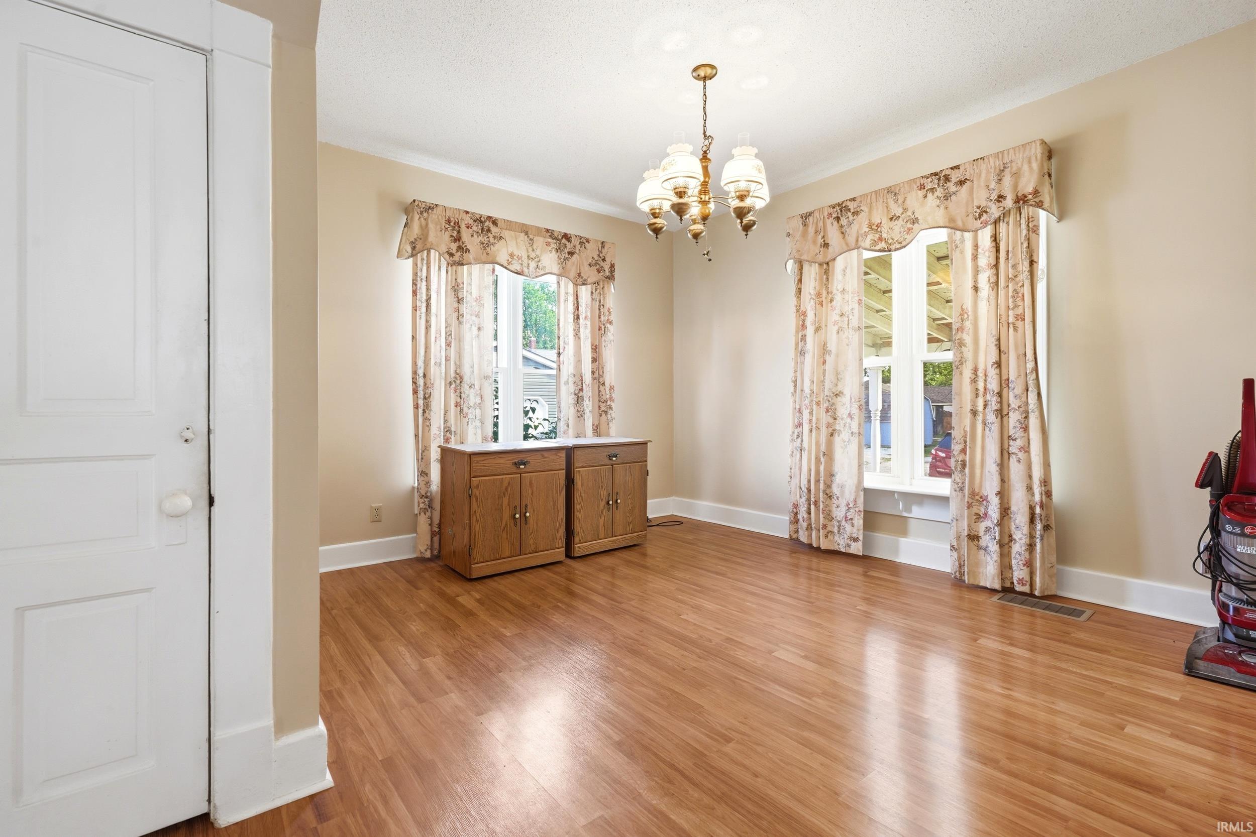 Spacious room featuring wood-finish flooring, two window openings, and a brass chandelier