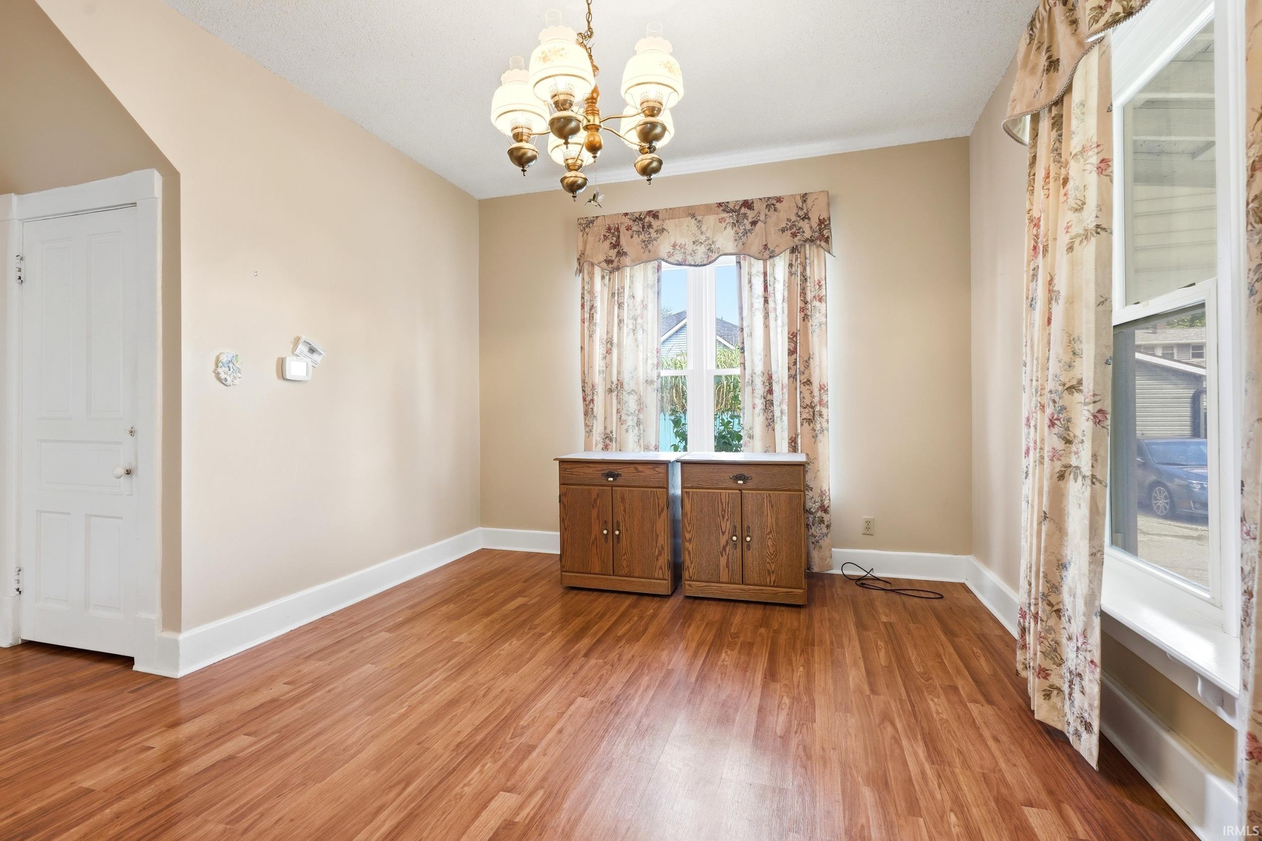 Spacious room featuring wood-finish flooring, light-toned walls, and a multi-bulb chandelier