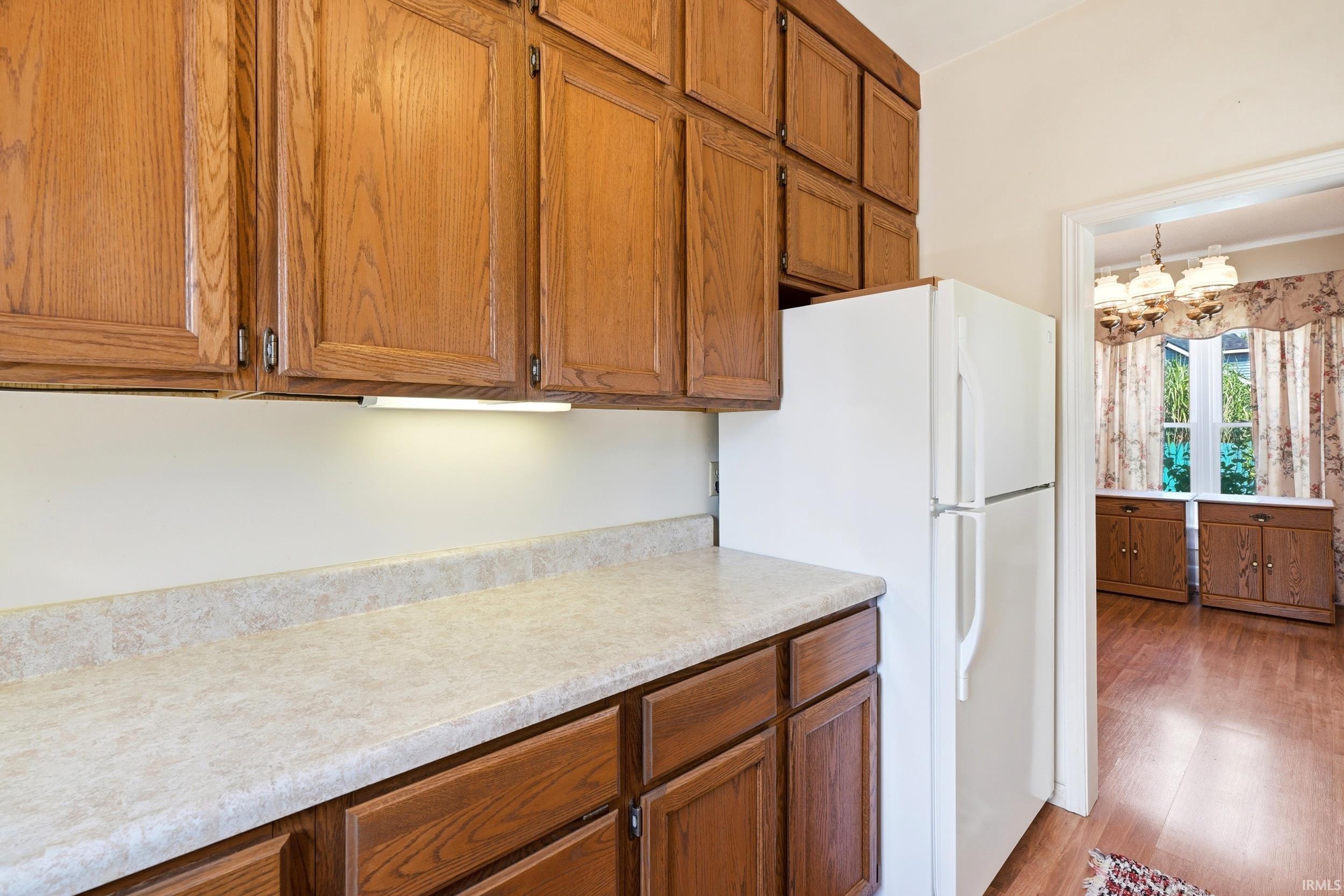 Kitchen featuring wood-finish cabinetry, light-toned countertops, under-cabinet lighting, and an included refrigerator