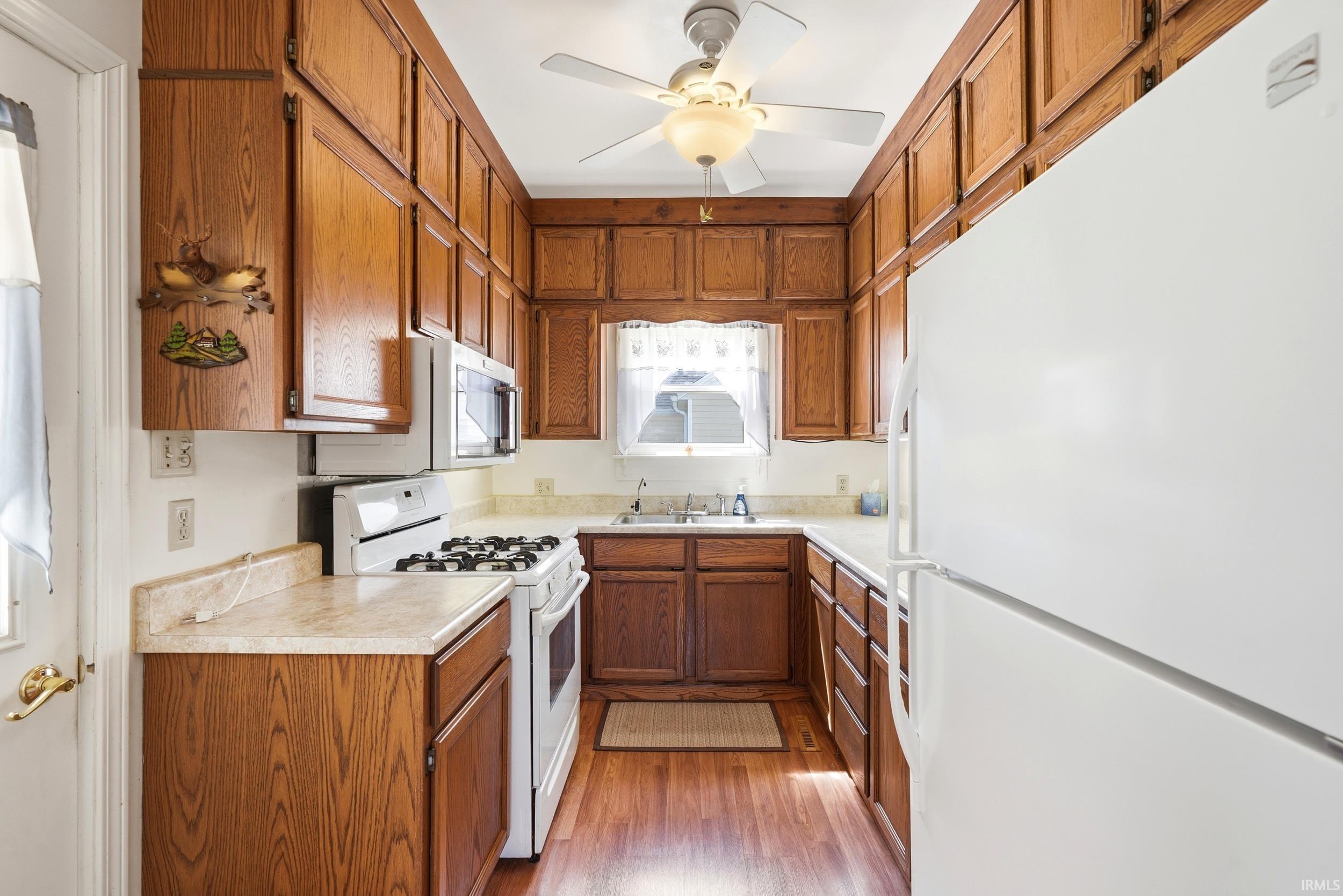 U-shaped kitchen featuring wood-finish cabinetry, white appliances, and wood-finish flooring