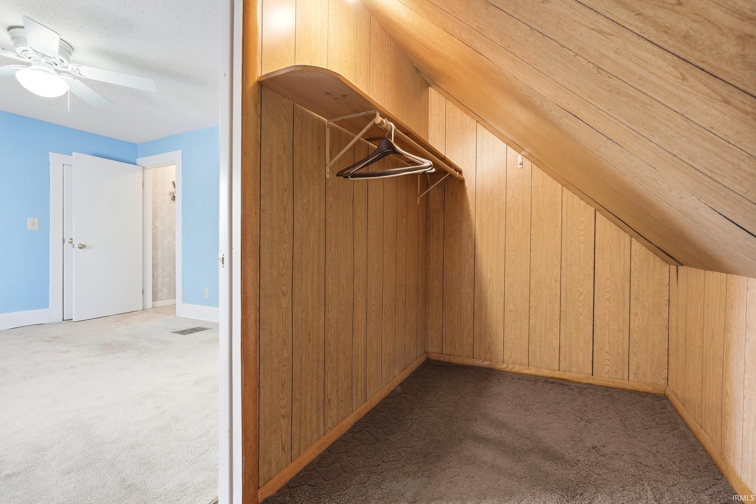 Wood-paneled closet featuring a clothing rod and sloped ceiling
