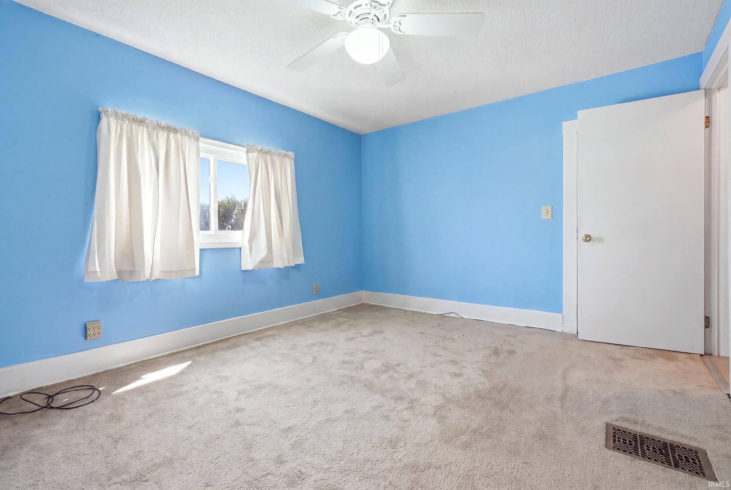 Carpeted interior room with light blue walls, a white ceiling fan, a window, a white door, and white trim