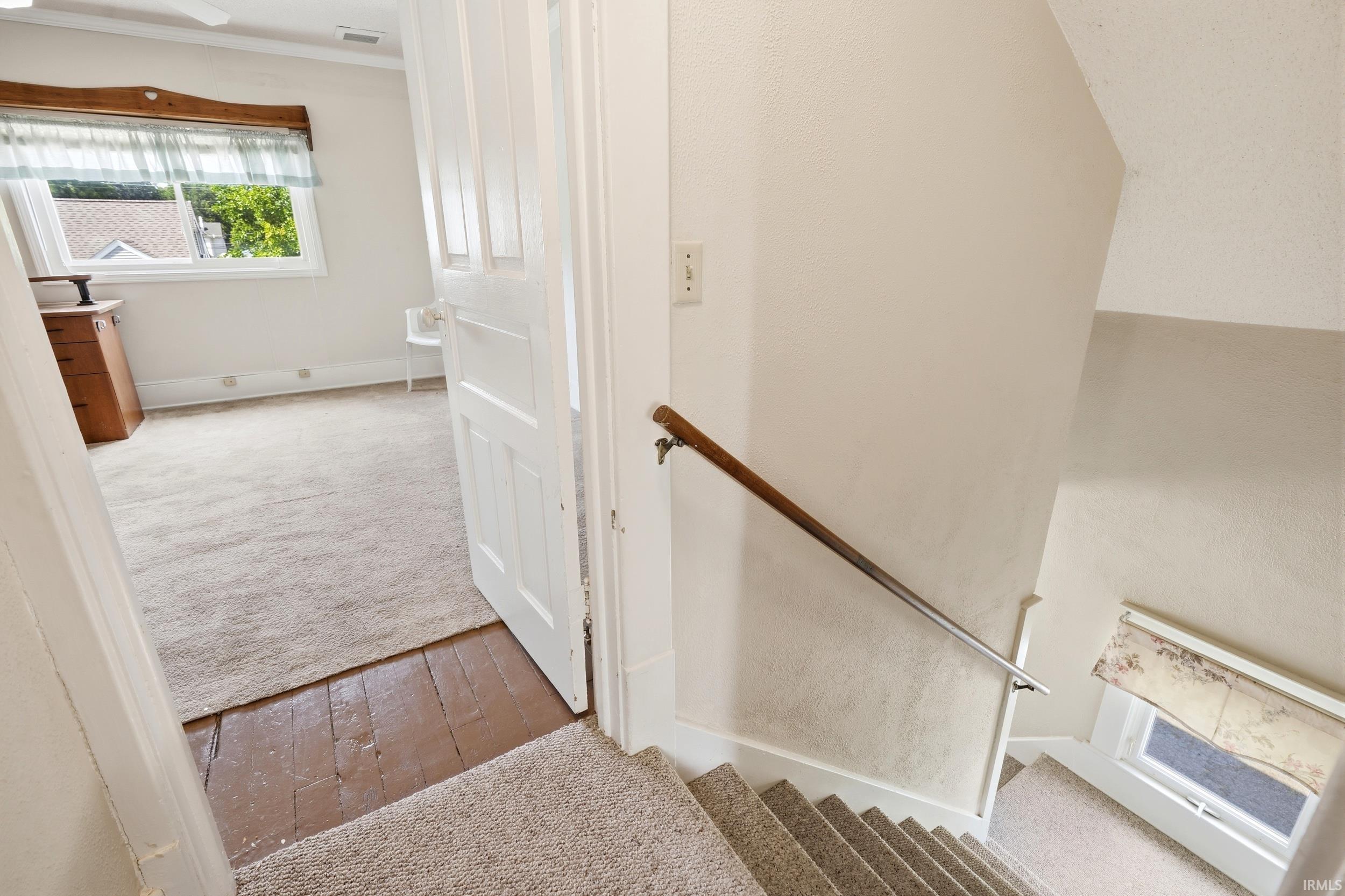 Carpeted staircase with a wood and metal handrail leading to a room with carpet over wood-finish flooring