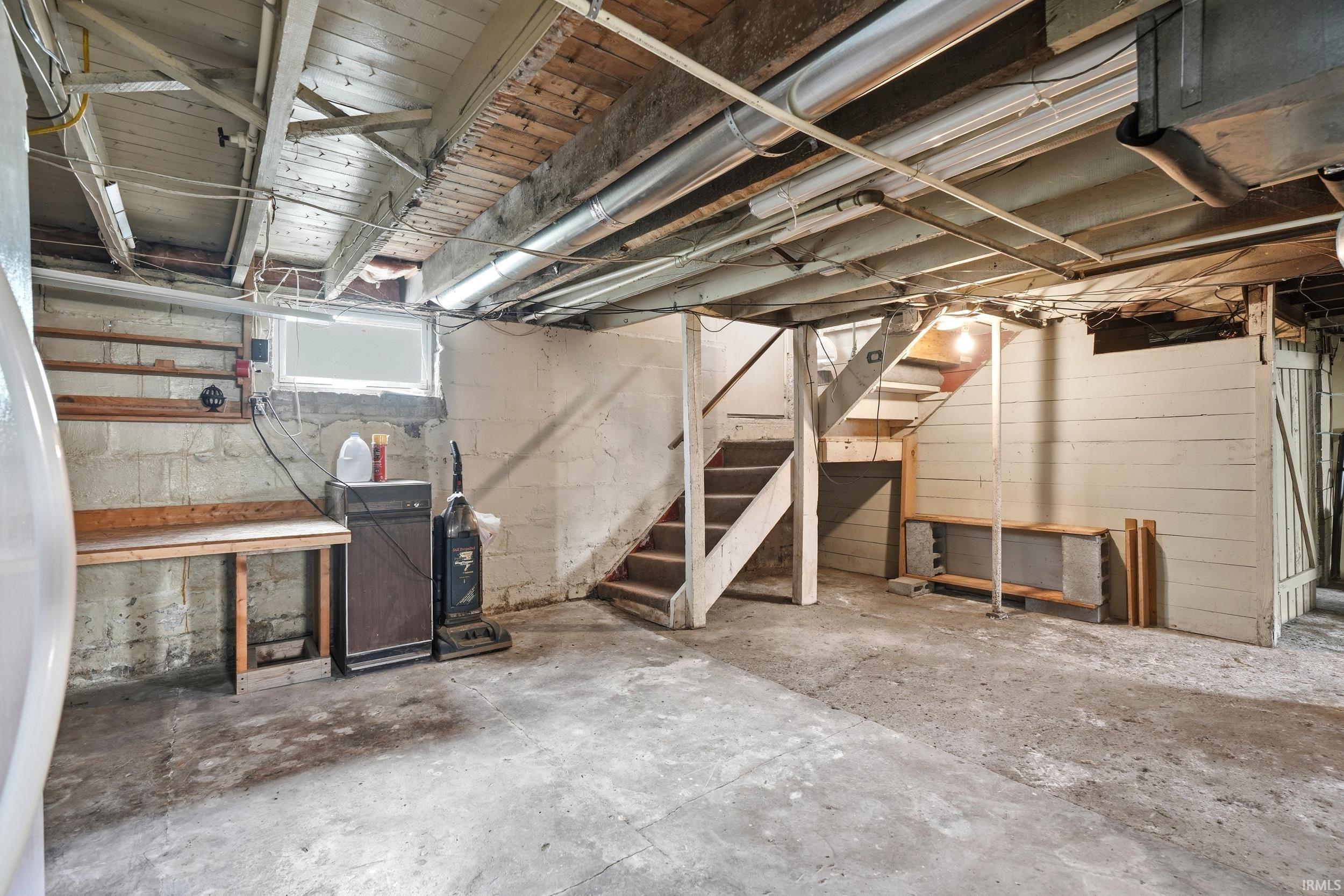 Unfinished basement featuring concrete flooring, exposed ceiling joists, wood stairs, and block walls