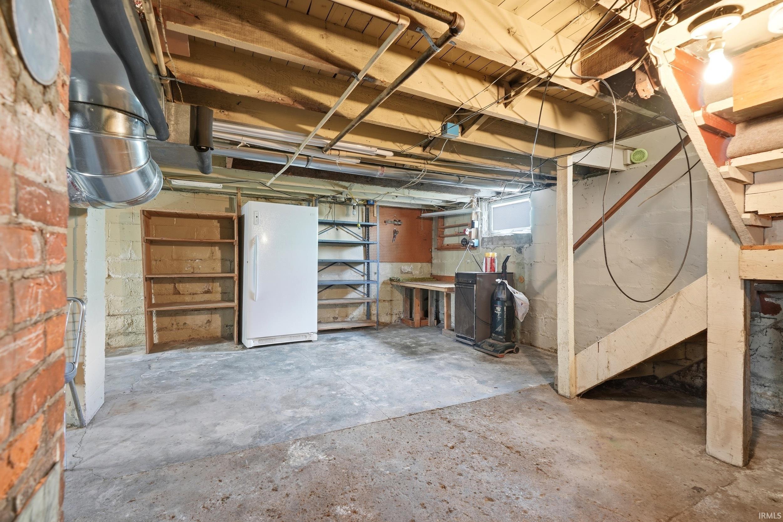 Spacious utility room featuring a concrete floor, exposed brick wall, and visible structural beams