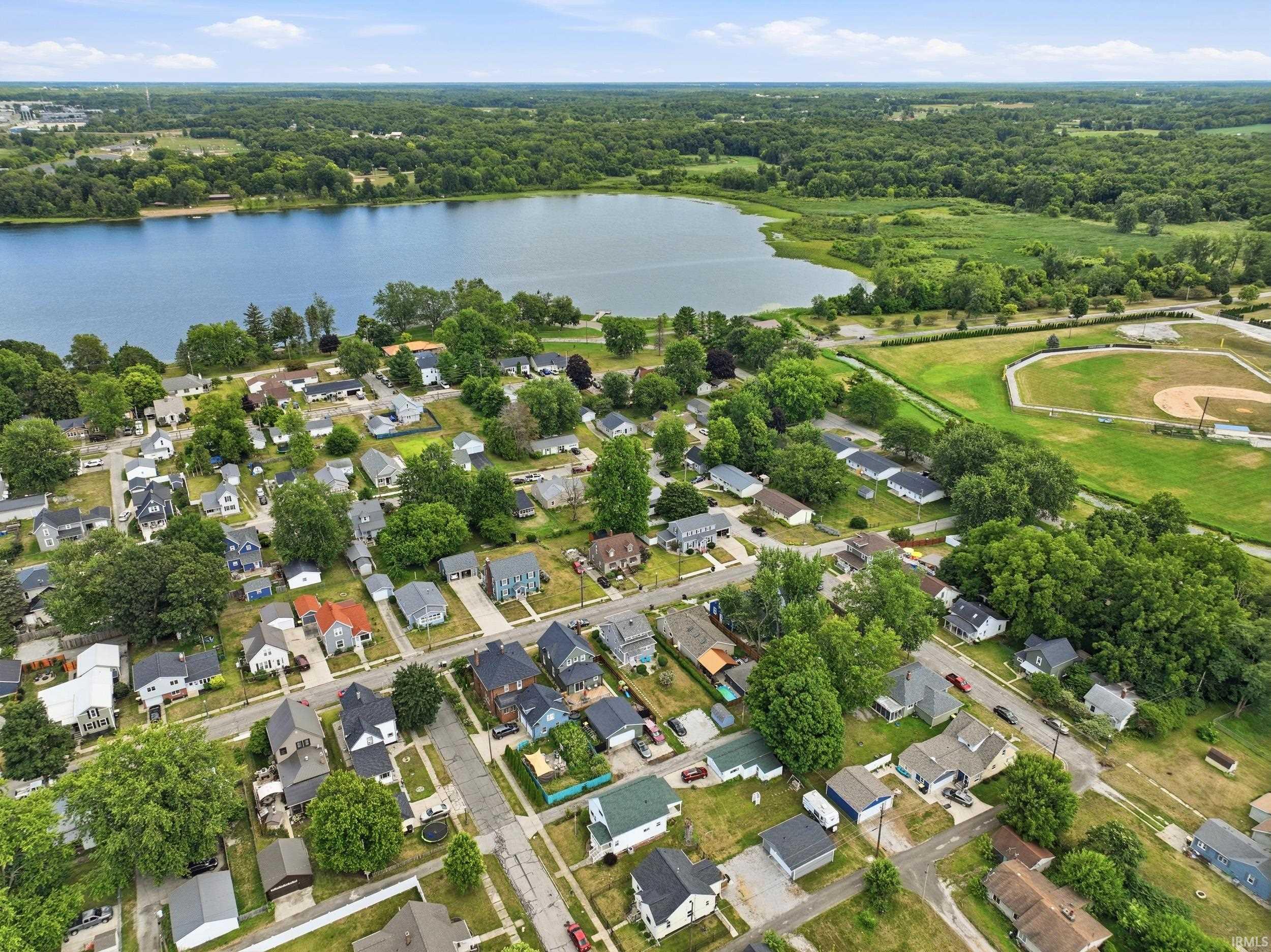Aerial perspective showcasing a residential neighborhood with a prominent lake, extensive green spaces, and a nearby sports field