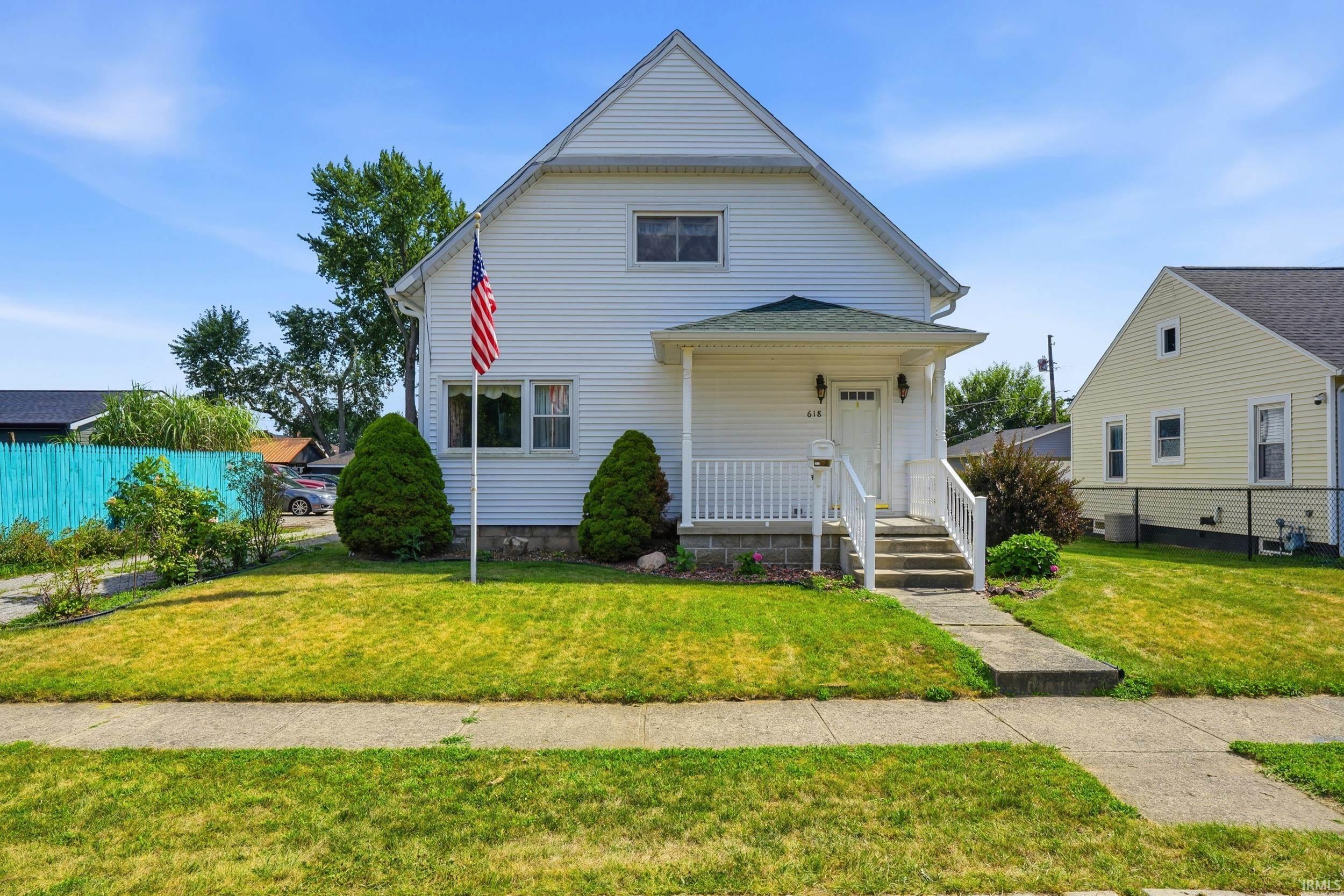 White siding exterior with a covered front porch, concrete walkway, and a manicured lawn