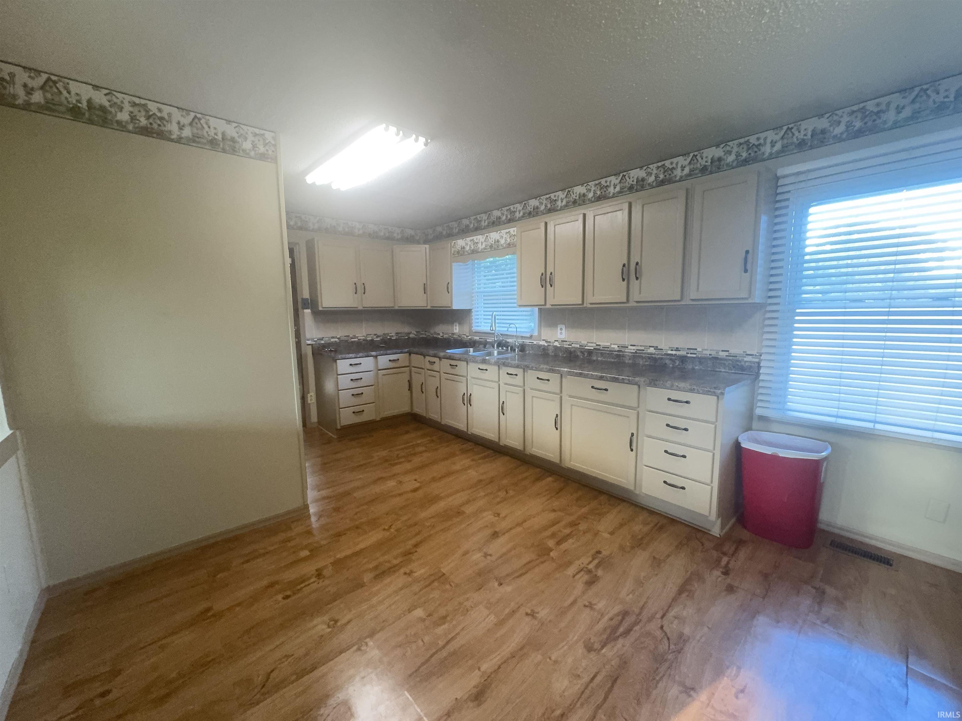 Spacious kitchen featuring cream-colored cabinetry with ample storage, wood-finish flooring throughout, granite countertops, and abundant natural light from multiple windows with blinds
