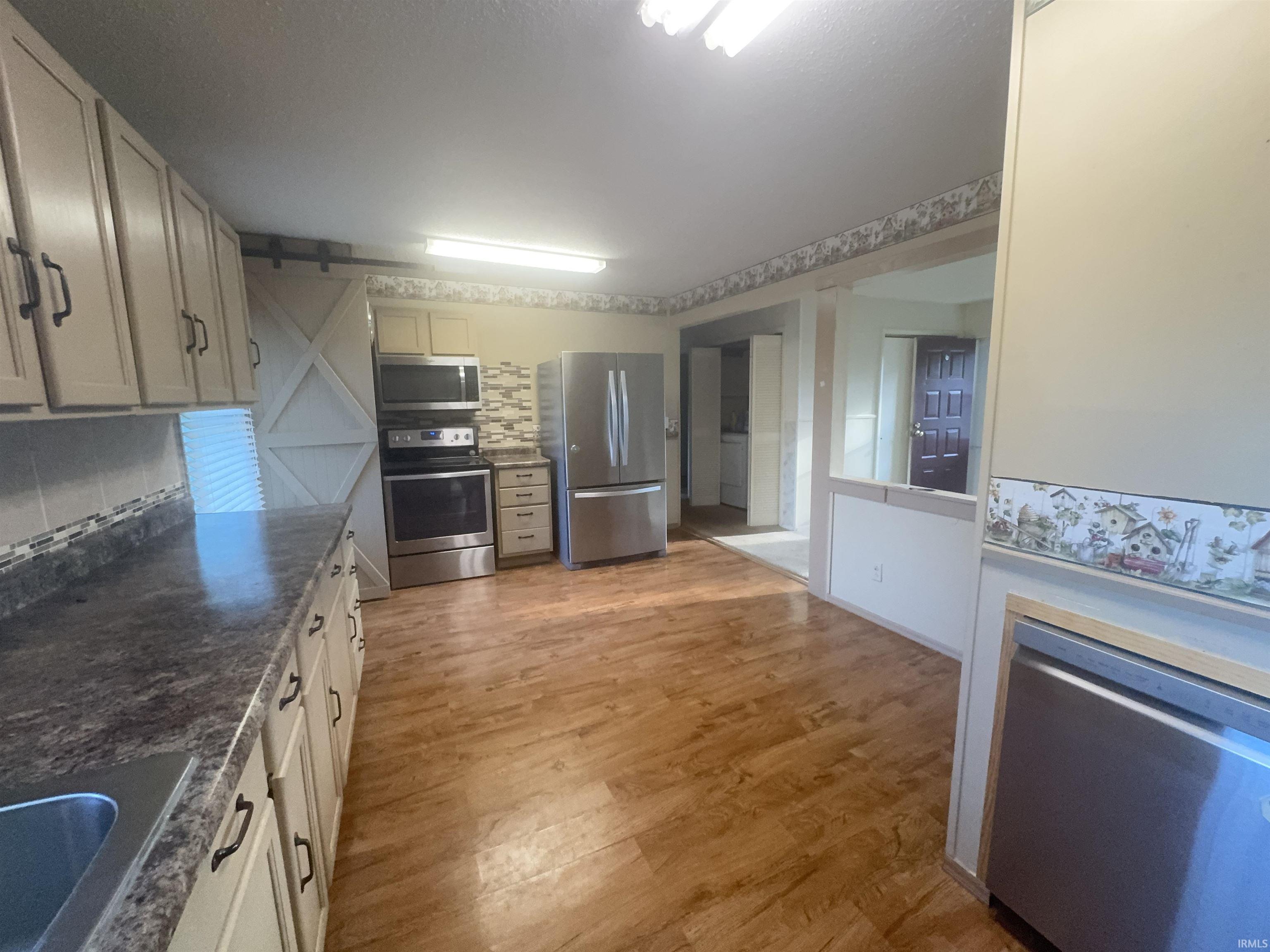 Spacious kitchen featuring cream cabinetry, wood-finish flooring, and stainless steel appliances including dual wall ovens, a refrigerator with matching finish, and a dishwasher