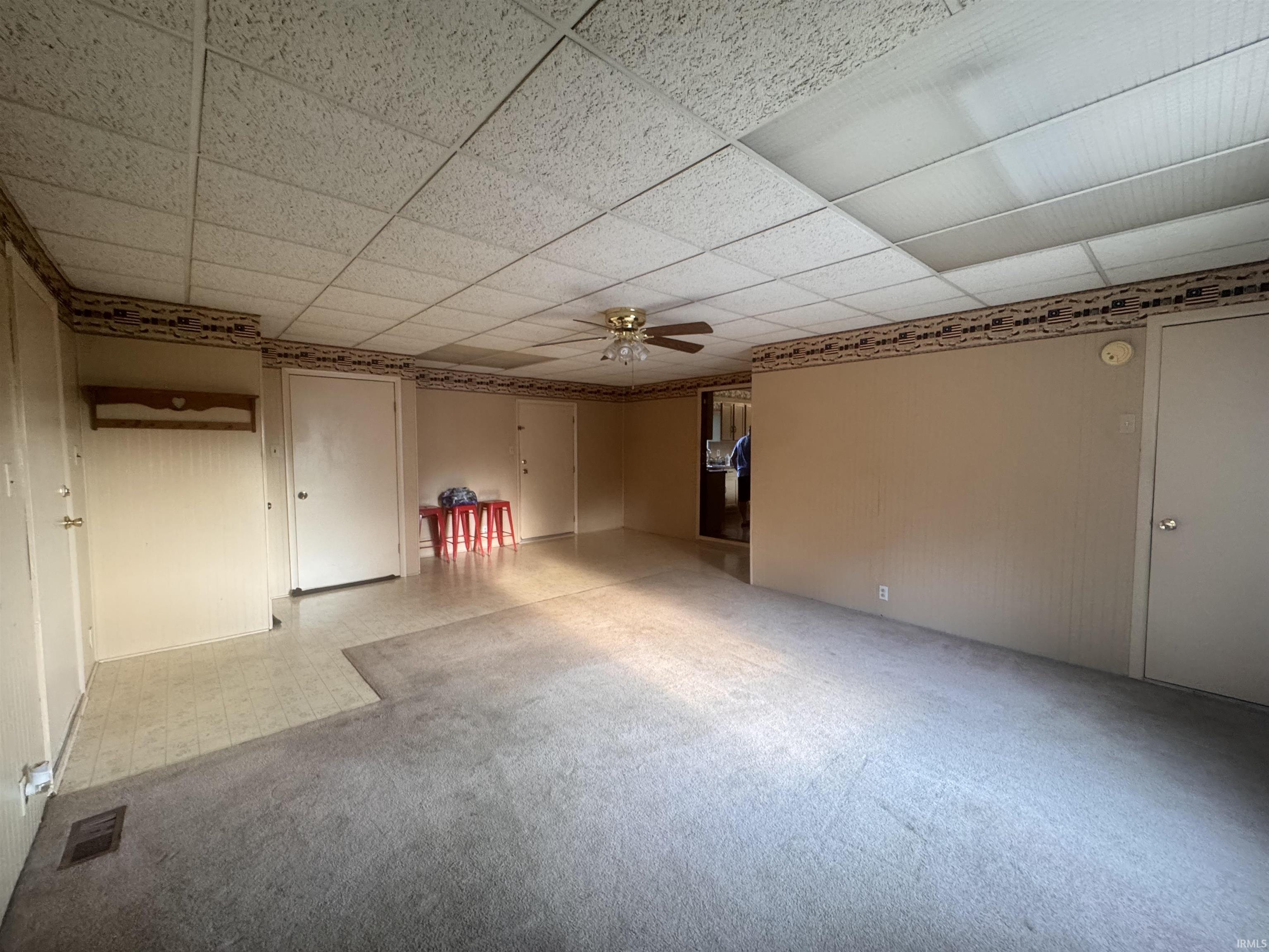 Spacious interior featuring a combination of carpet and vinyl flooring, neutral wall tones, and a paneled ceiling