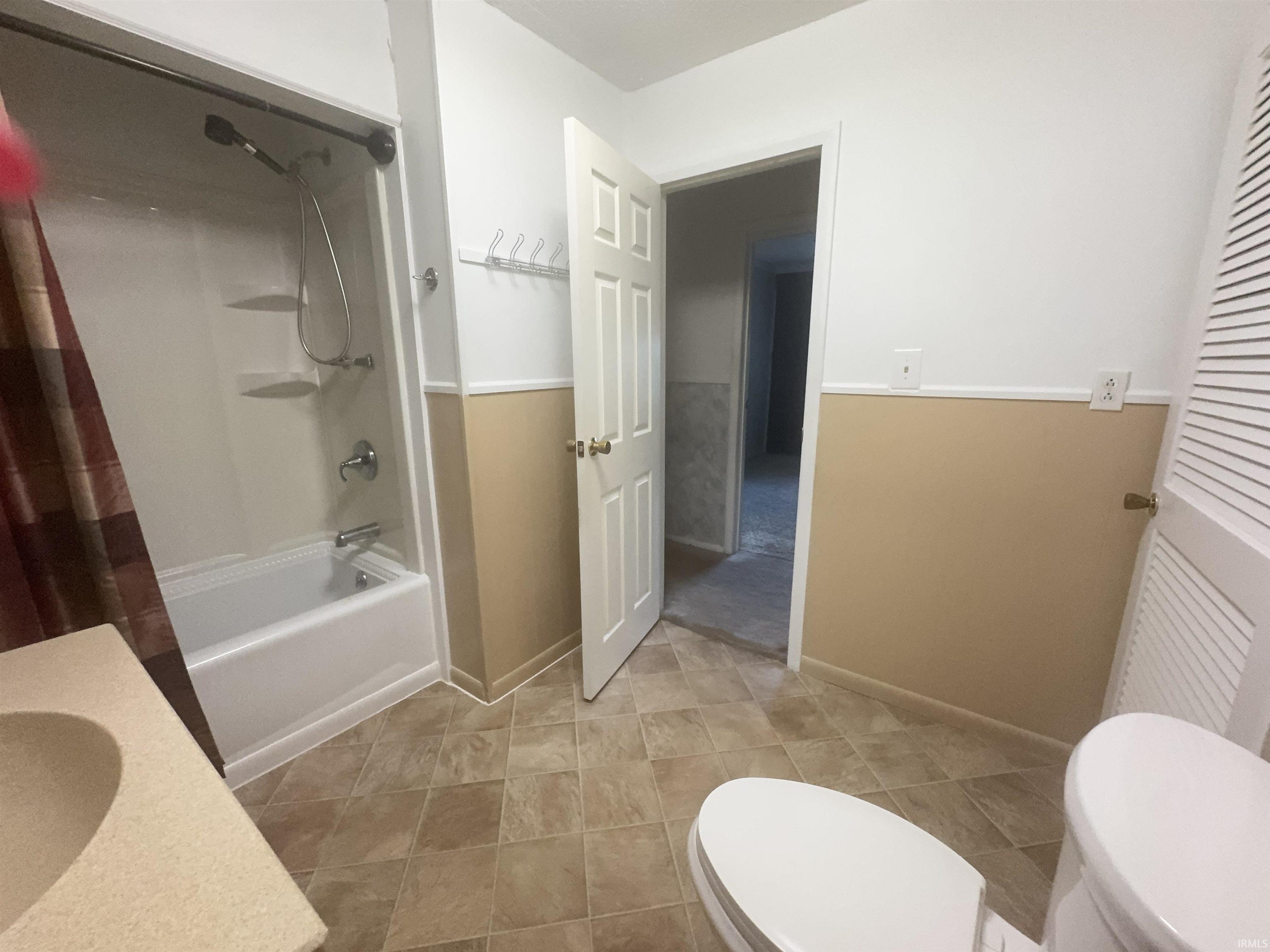 Bathroom featuring a white tub/shower combination with a single-handle faucet, a light-colored vanity with an integrated sink, a commode, and patterned tile flooring