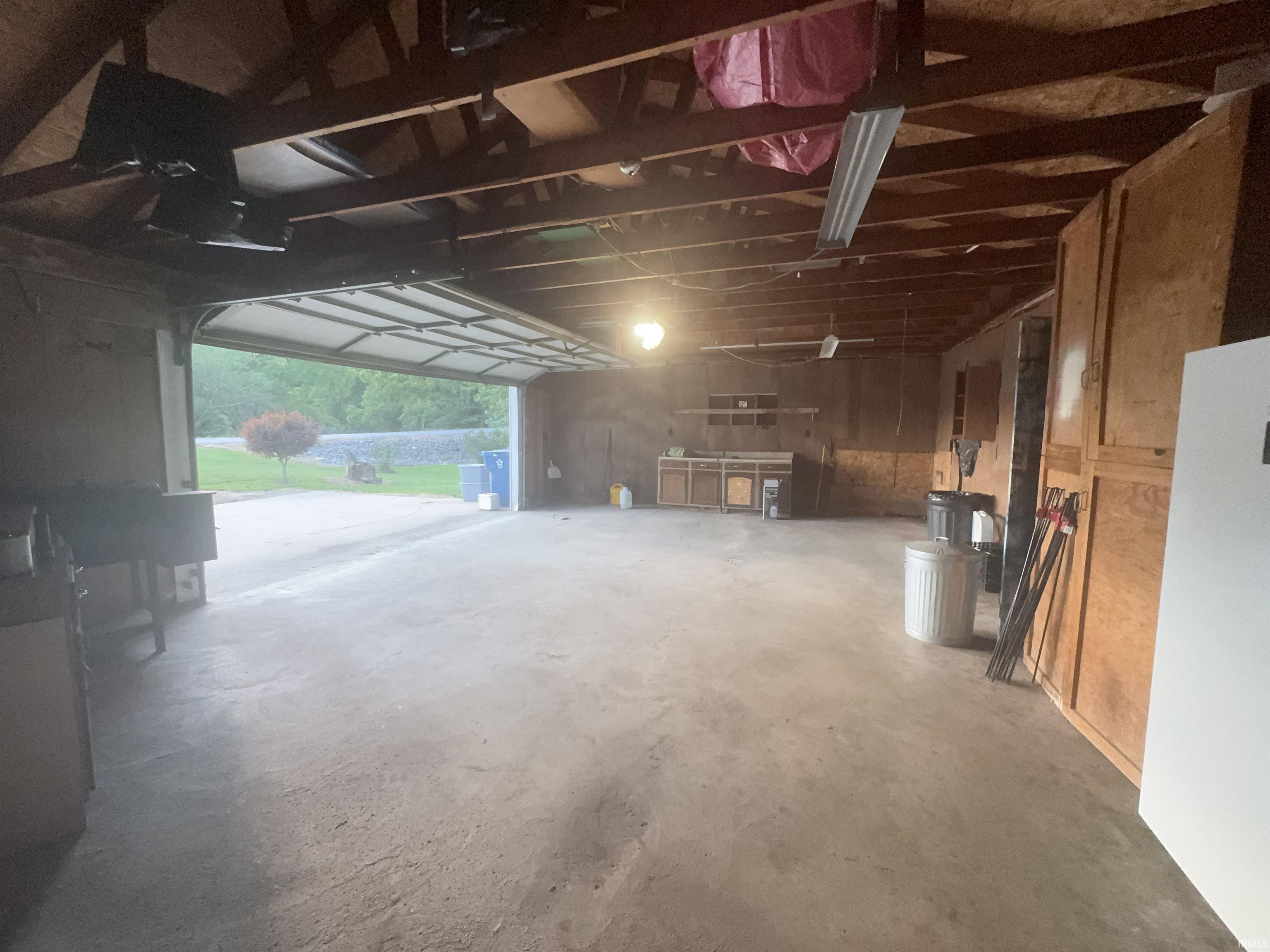 Spacious garage featuring a concrete floor, exposed wood beam ceiling, and a large overhead door