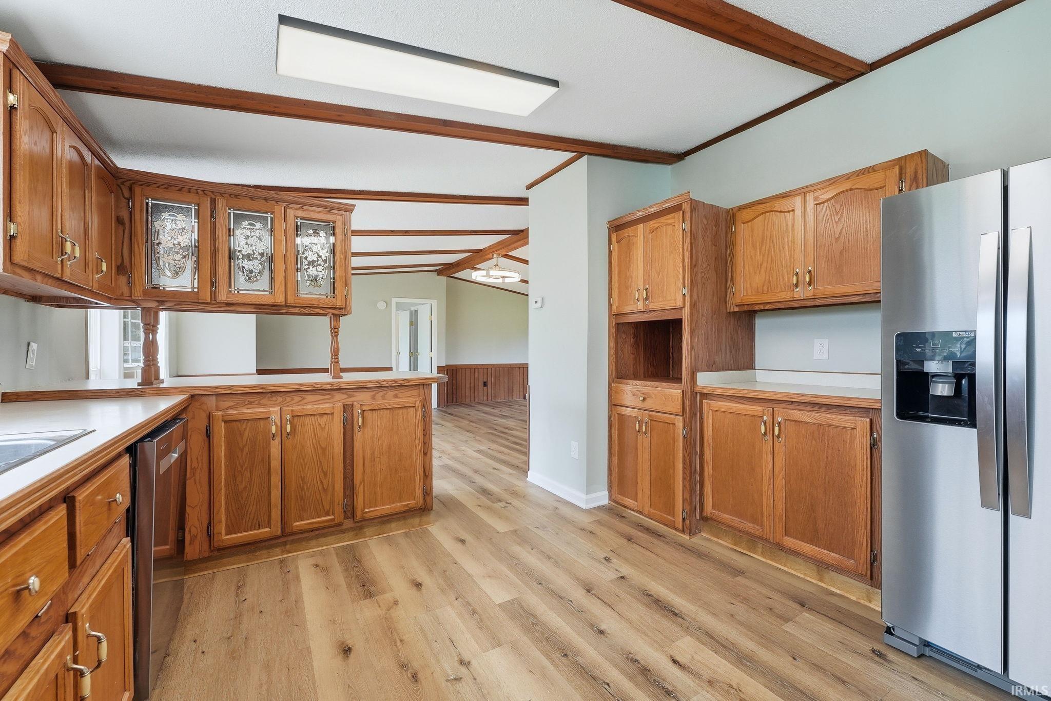 Kitchen featuring wood-finish flooring, extensive wood cabinetry, light-toned countertops, and a stainless steel refrigerator